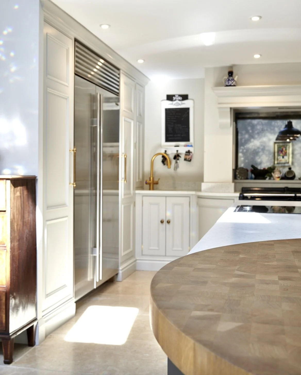 A kitchen with white cabinetry, a stainless steel refrigerator, a wooden countertop, a gold faucet, and various decorative items.