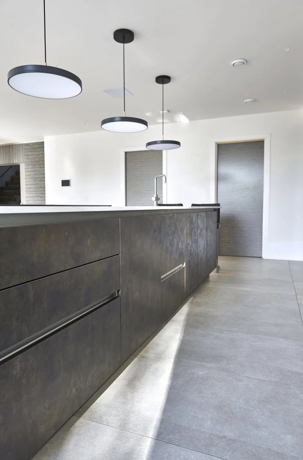 Modern kitchen with dark wood cabinets, gray tile flooring, and three round black and white pendant lights hanging from the ceiling.