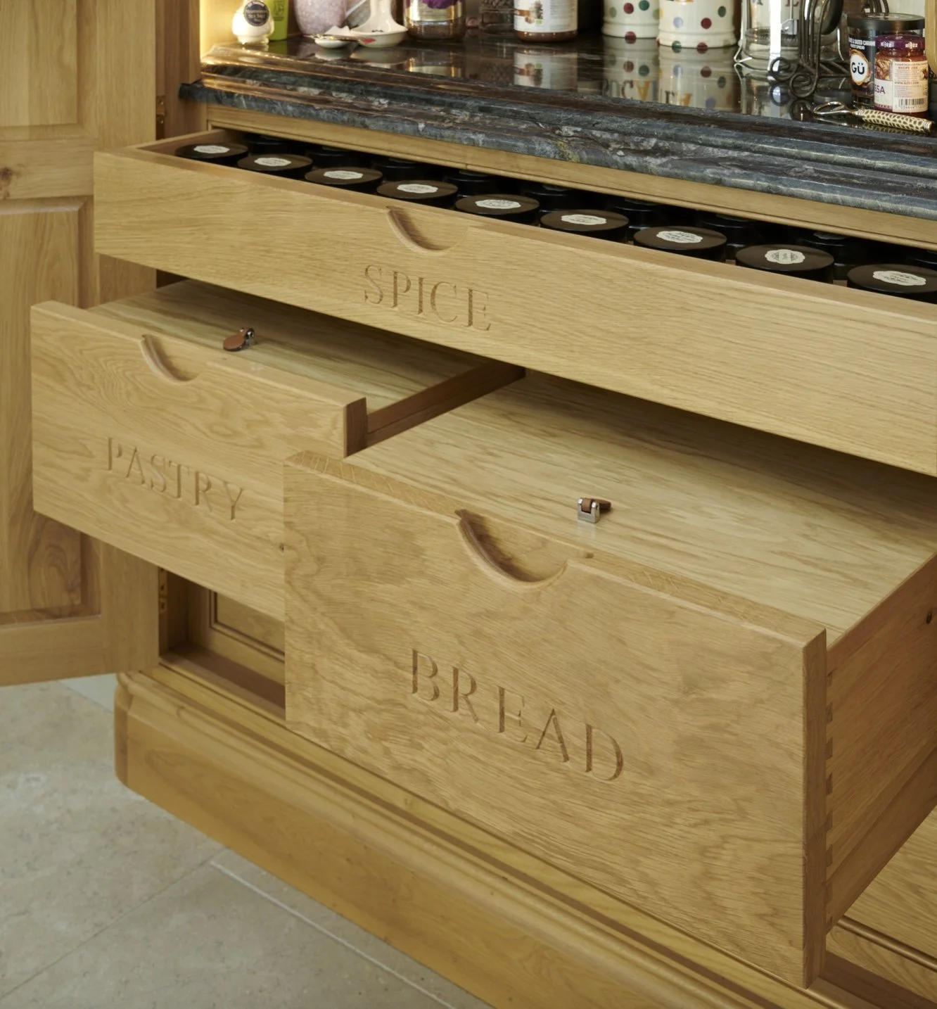 Wooden kitchen drawers labeled 'Spice,' 'Pasty,' and 'Bread' with cutout handles, partially open, with the Spice drawer extended.