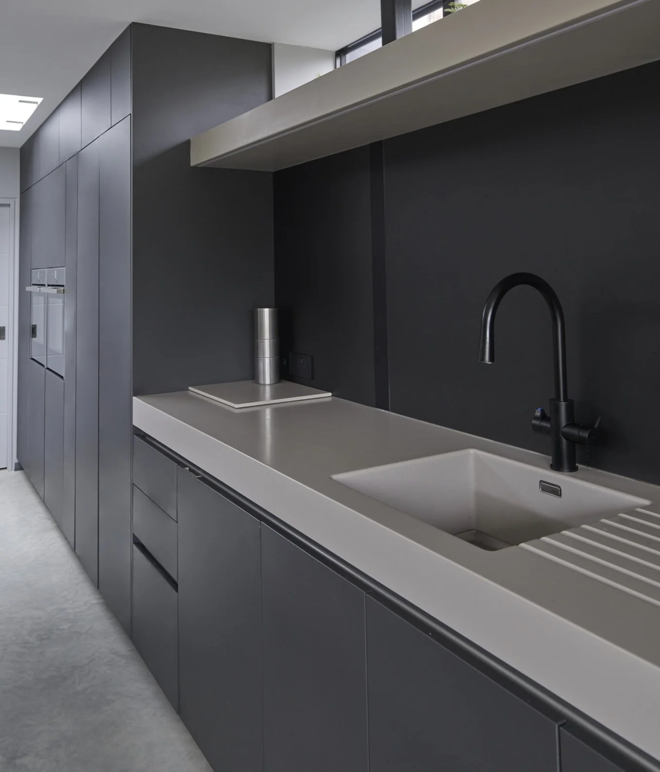 Modern kitchen with dark cabinets, a black faucet, a sink, and a gray countertop with a white backsplash