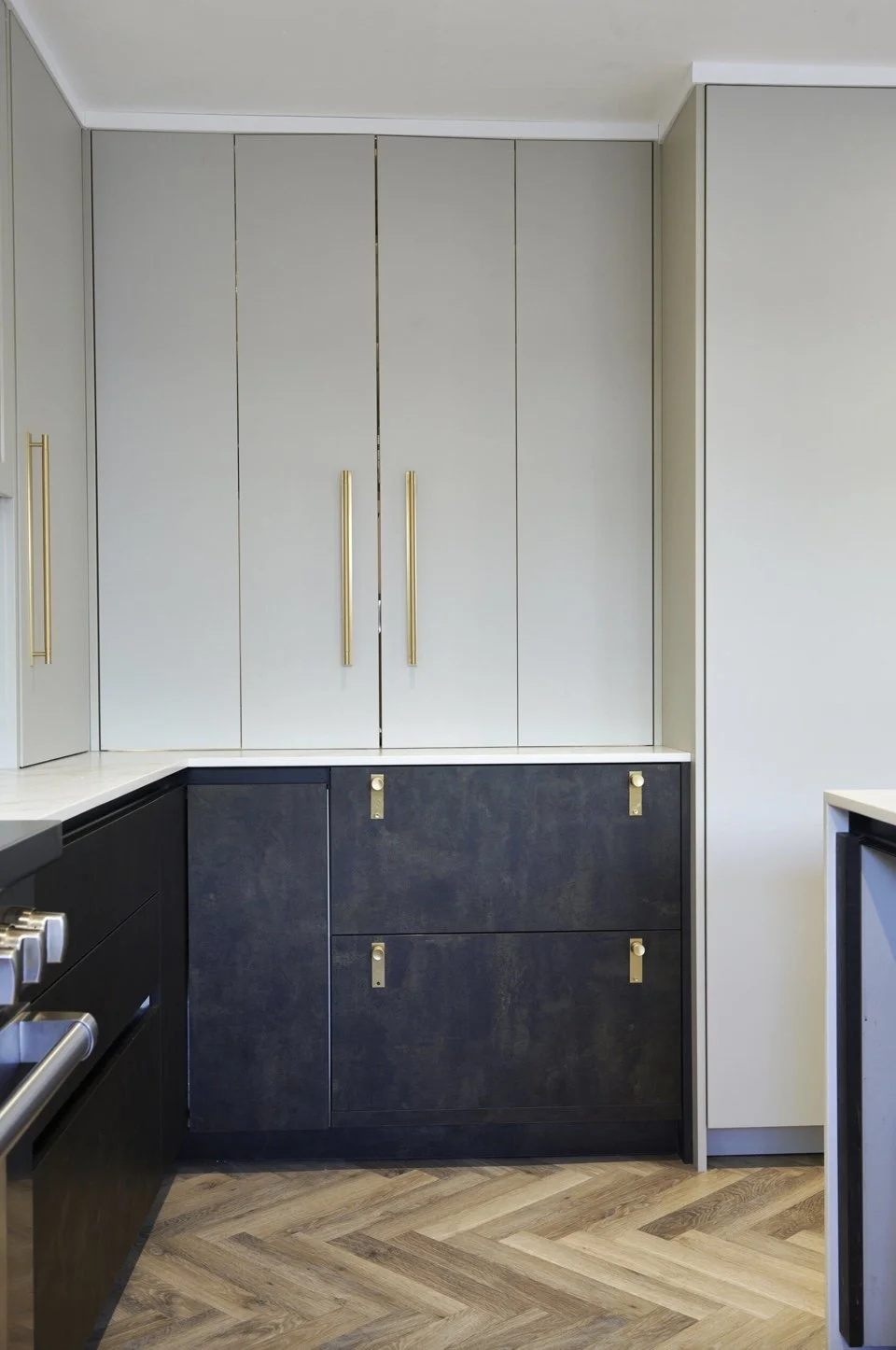 Kitchen with gray and black cabinets, gold handles, and a herringbone wood floor.