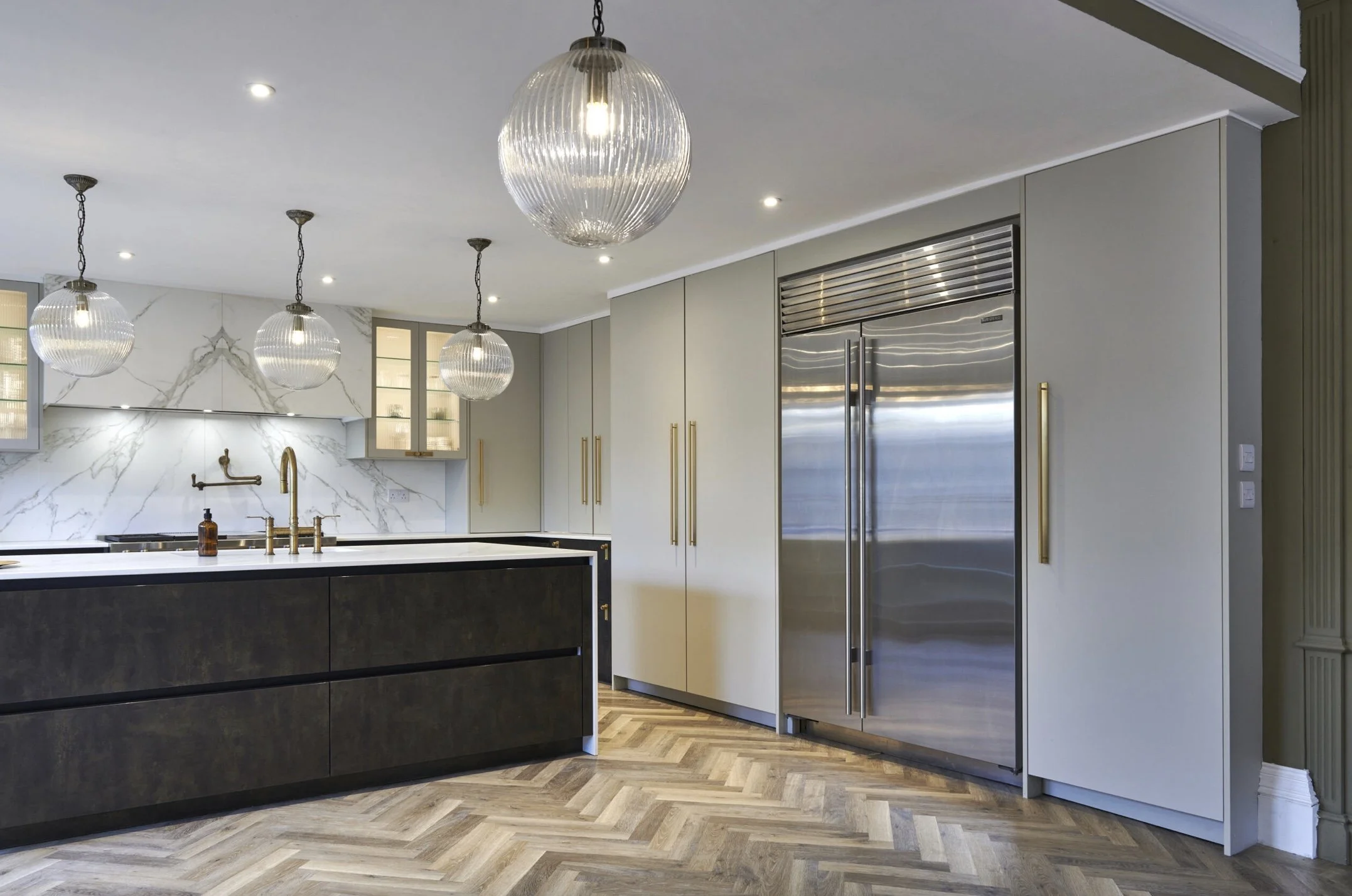 Modern kitchen with white and black cabinetry, stainless steel refrigerator, marble backsplash, and three glass pendant lights.