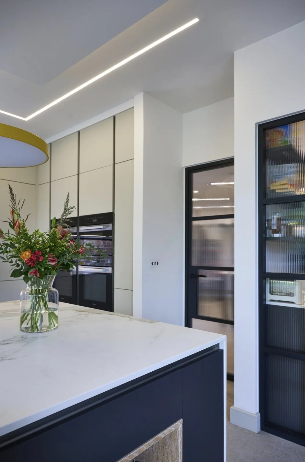Modern kitchen with white and black cabinetry, a marble countertop, a glass vase with flowers, and textured glass cabinet doors.
