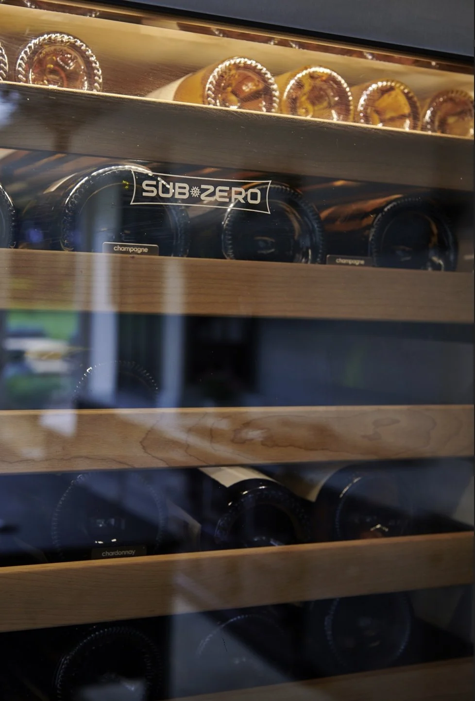 A wine cooler filled with bottles of champagne and chardonnay, with a glass door and wooden shelves.