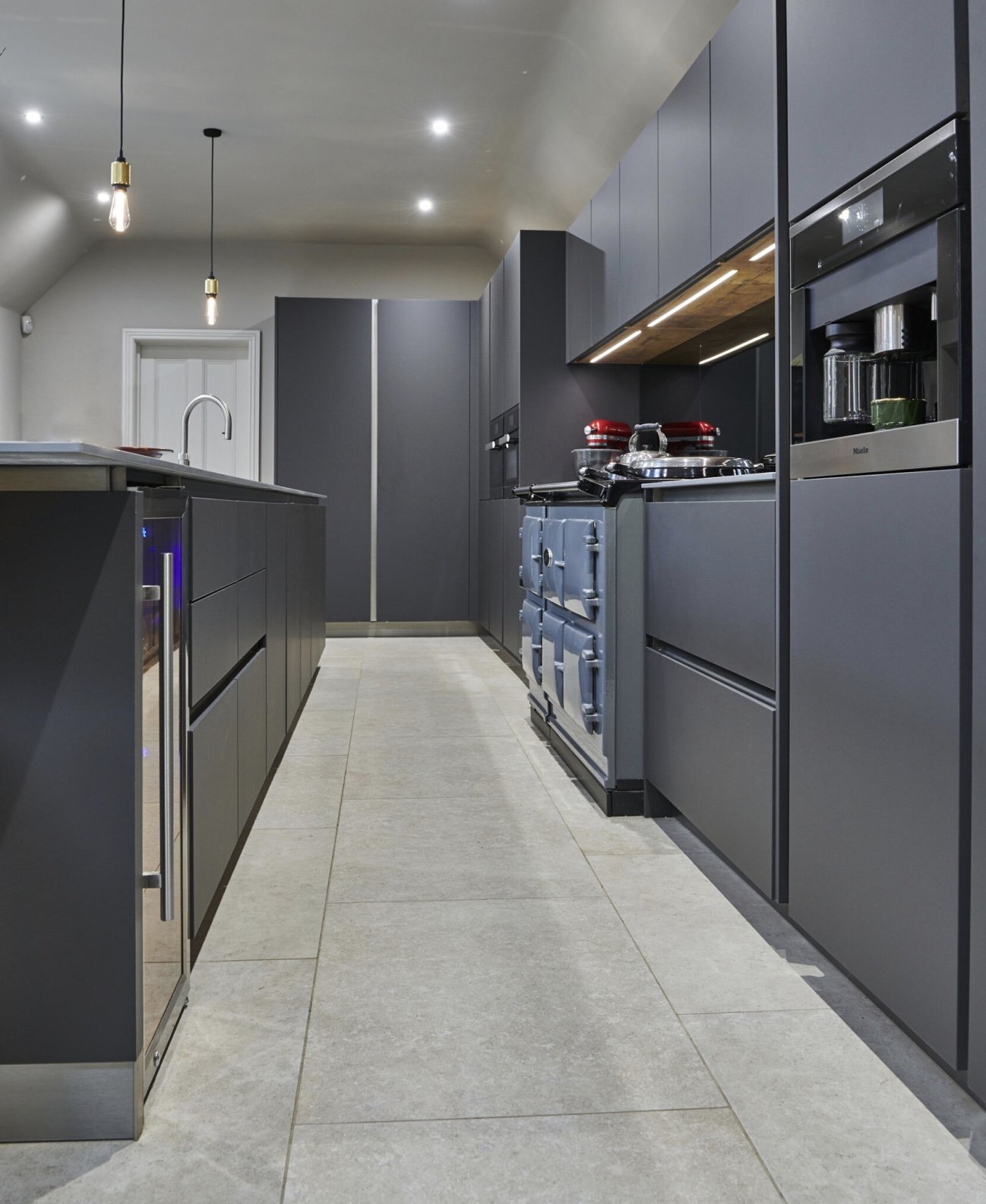 Modern kitchen with gray cabinets, black countertops, stainless steel appliances, and pendant and recessed lighting.