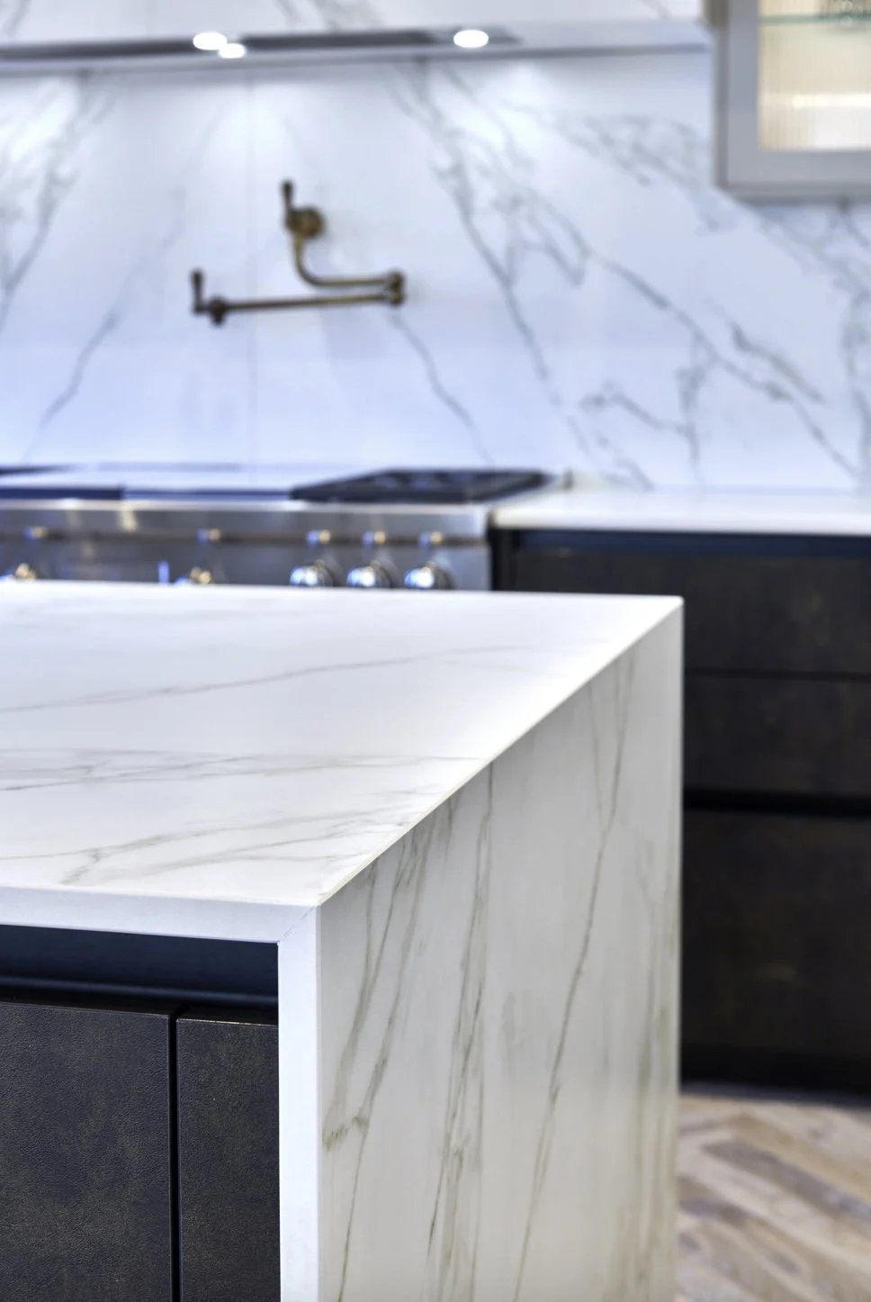 Close-up of a white marble kitchen island with subtle gray veining, with a stove and kitchen countertop in the background.