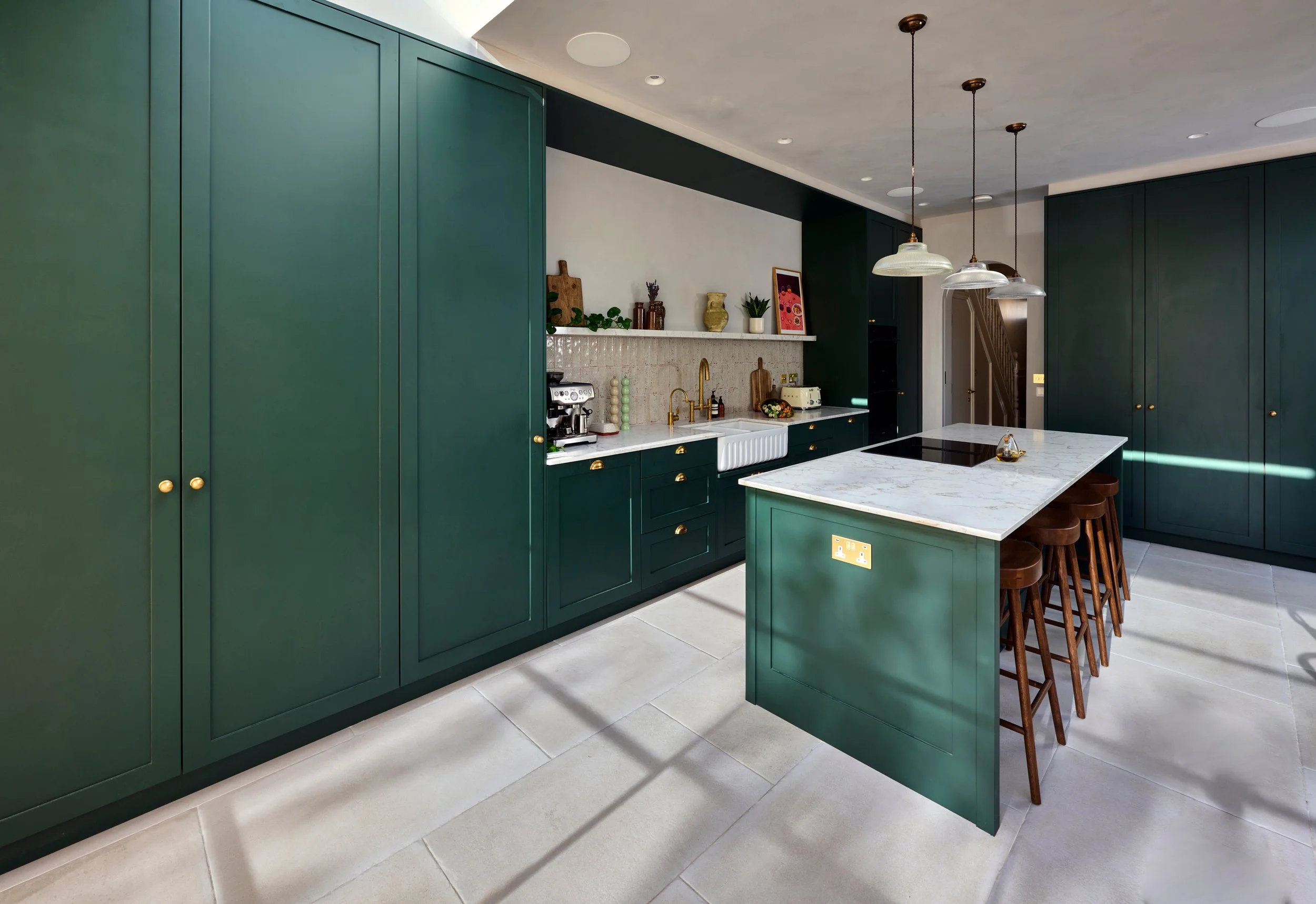 Modern kitchen with dark green cabinets, white marble countertops, and pendant lighting over an island with bar stools.