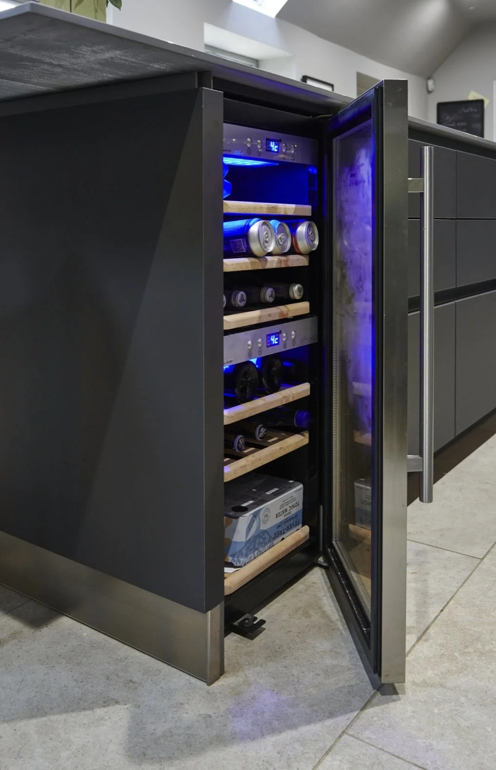 Open wine and beer cooler with cans inside, wooden shelves, and a digital temperature display set to 4°C, positioned in a modern kitchen.