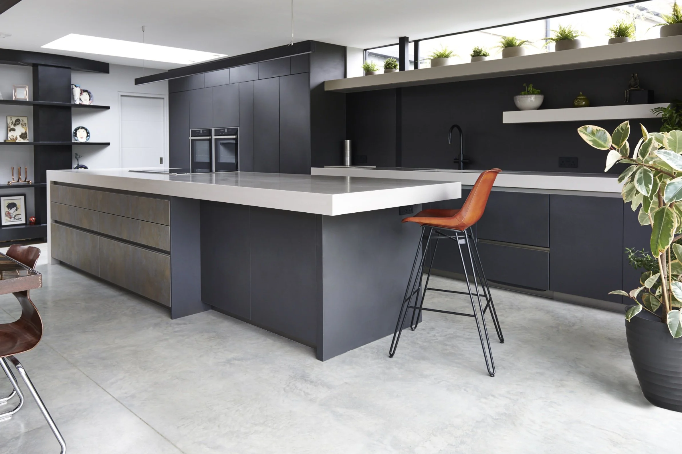 Modern kitchen with black cabinetry and white countertops, a large island with a metallic front, and a brown barstool with a black metal frame.