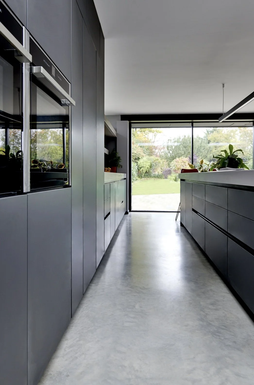 Modern kitchen with gray cabinetry and large windows overlooking a garden.