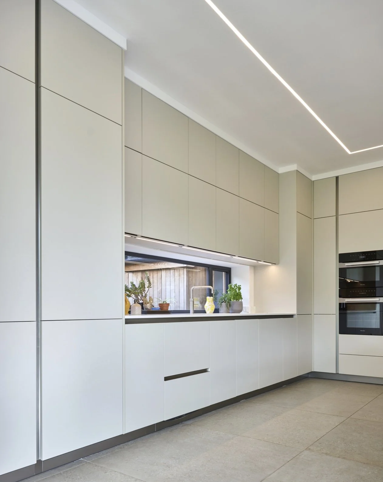 Modern kitchen with white cabinets, black countertop, potted plants on window sill, and built-in ovens.