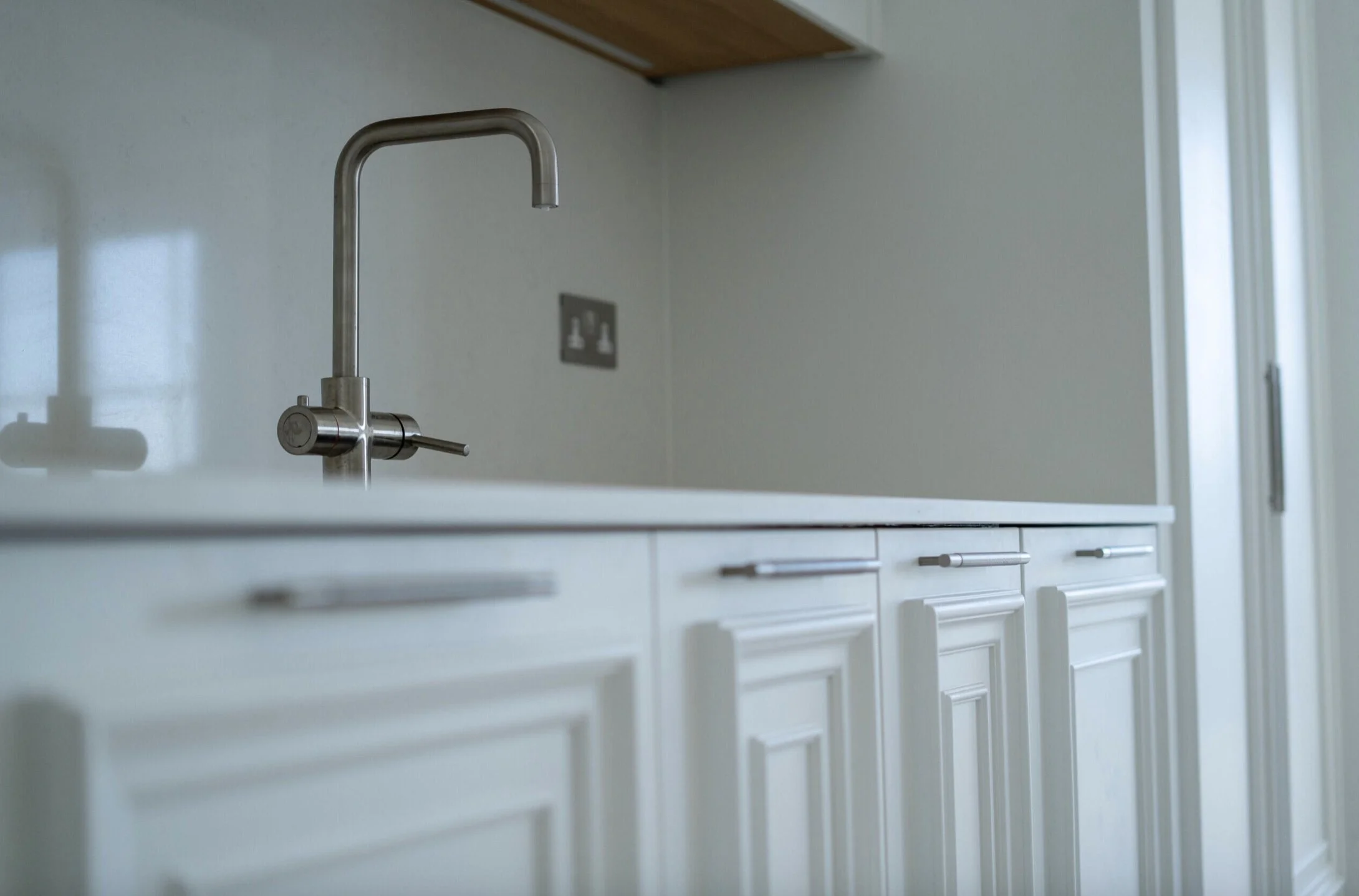 A modern kitchen sink with a stainless steel faucet above white cabinetry, in a well-lit room with a window on the right.