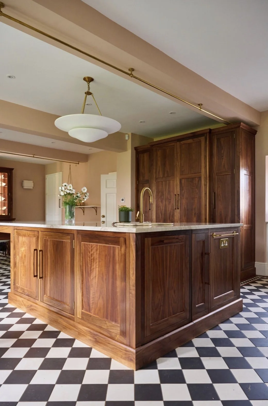 A kitchen with wooden cabinets, a marble countertop, a brass faucet, and checkered black and white floor tiles.