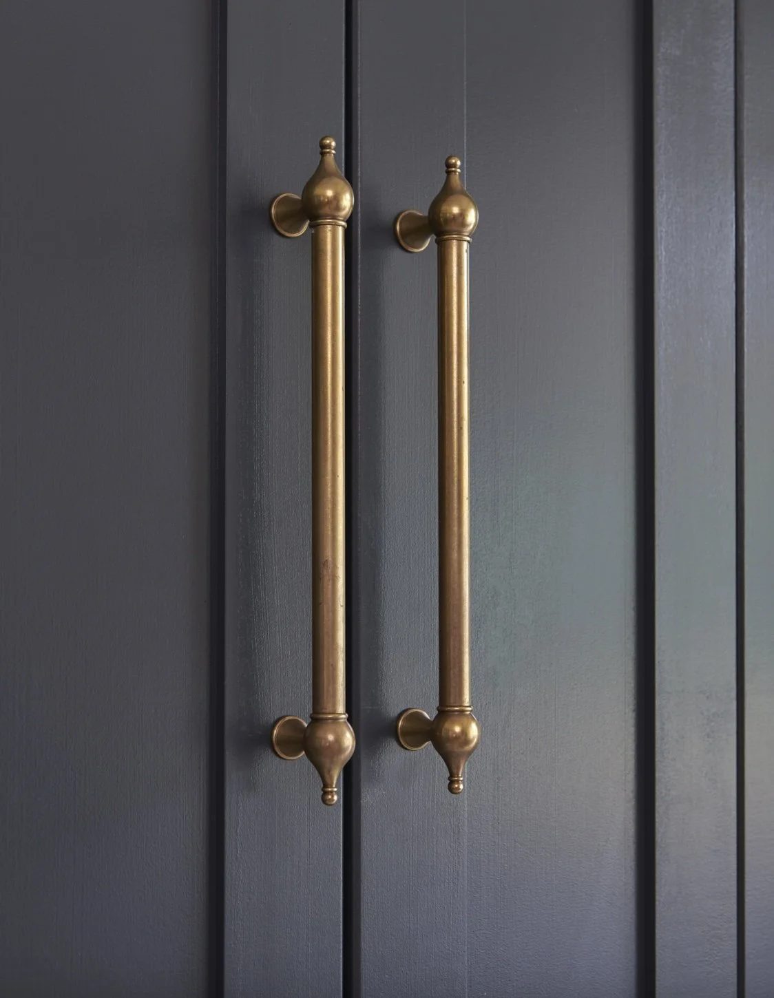 Close-up of two vertical brass door handles mounted on a dark gray wooden door.