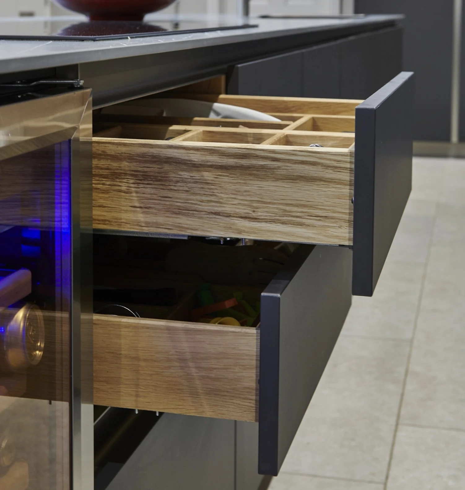 Wooden kitchen drawers open with various utensils inside, situated below a countertop.