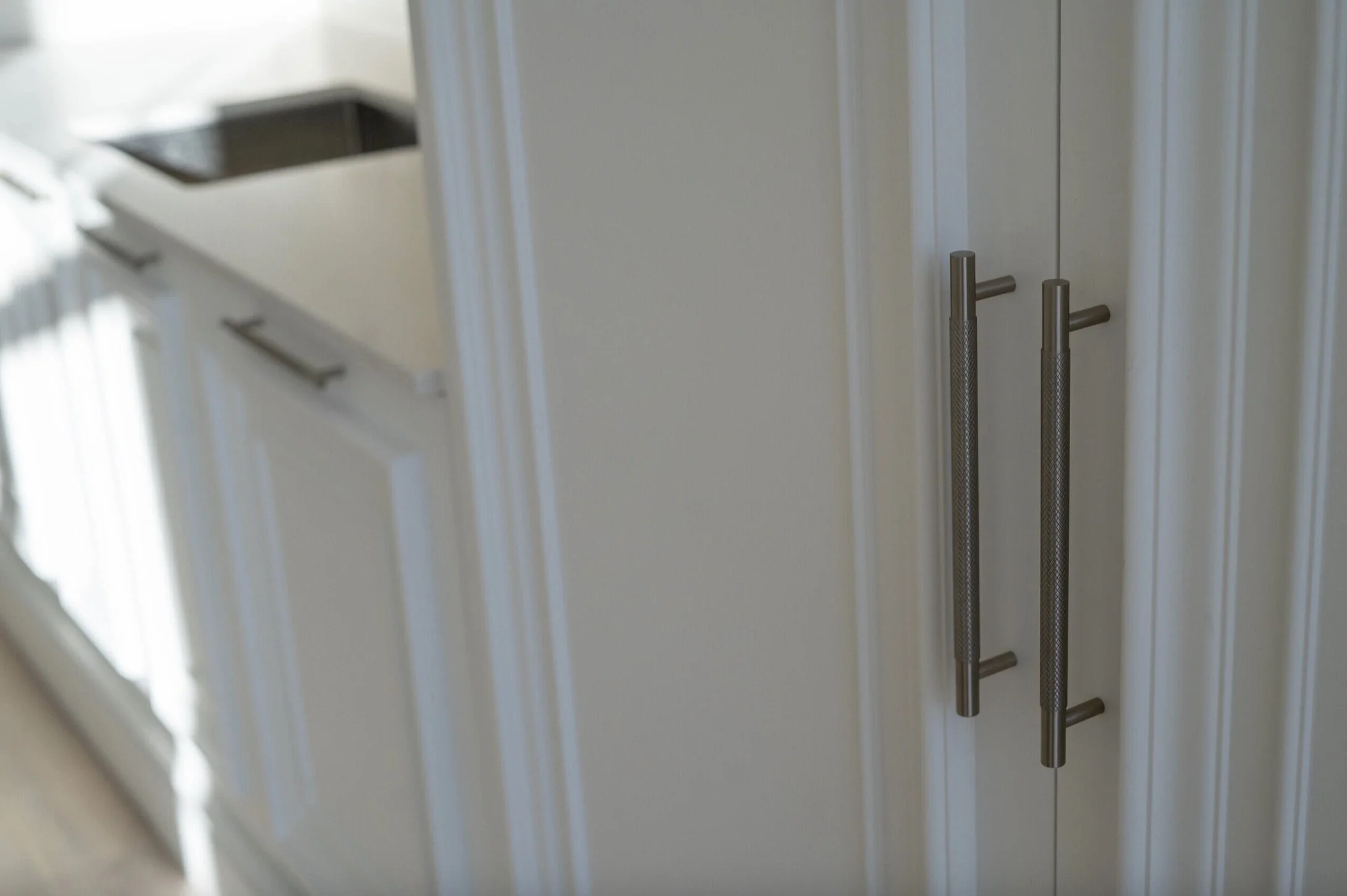 Close-up of white kitchen cabinets with metal handles, a white countertop, and a black kitchen sink.