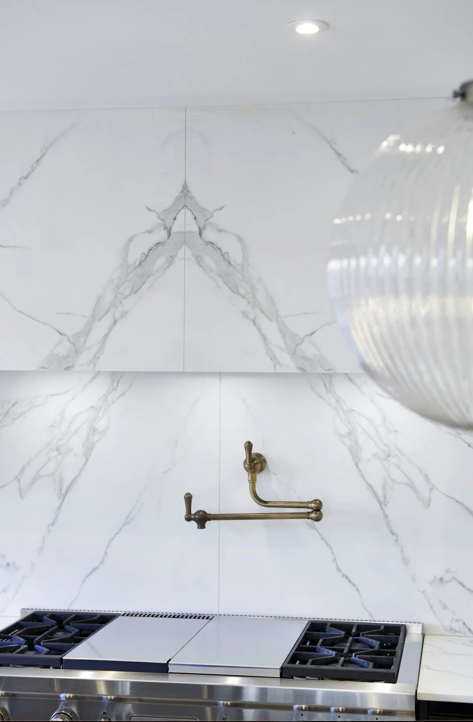A kitchen with a marble backsplash, a brass faucet, and a gas stove with four burners.
