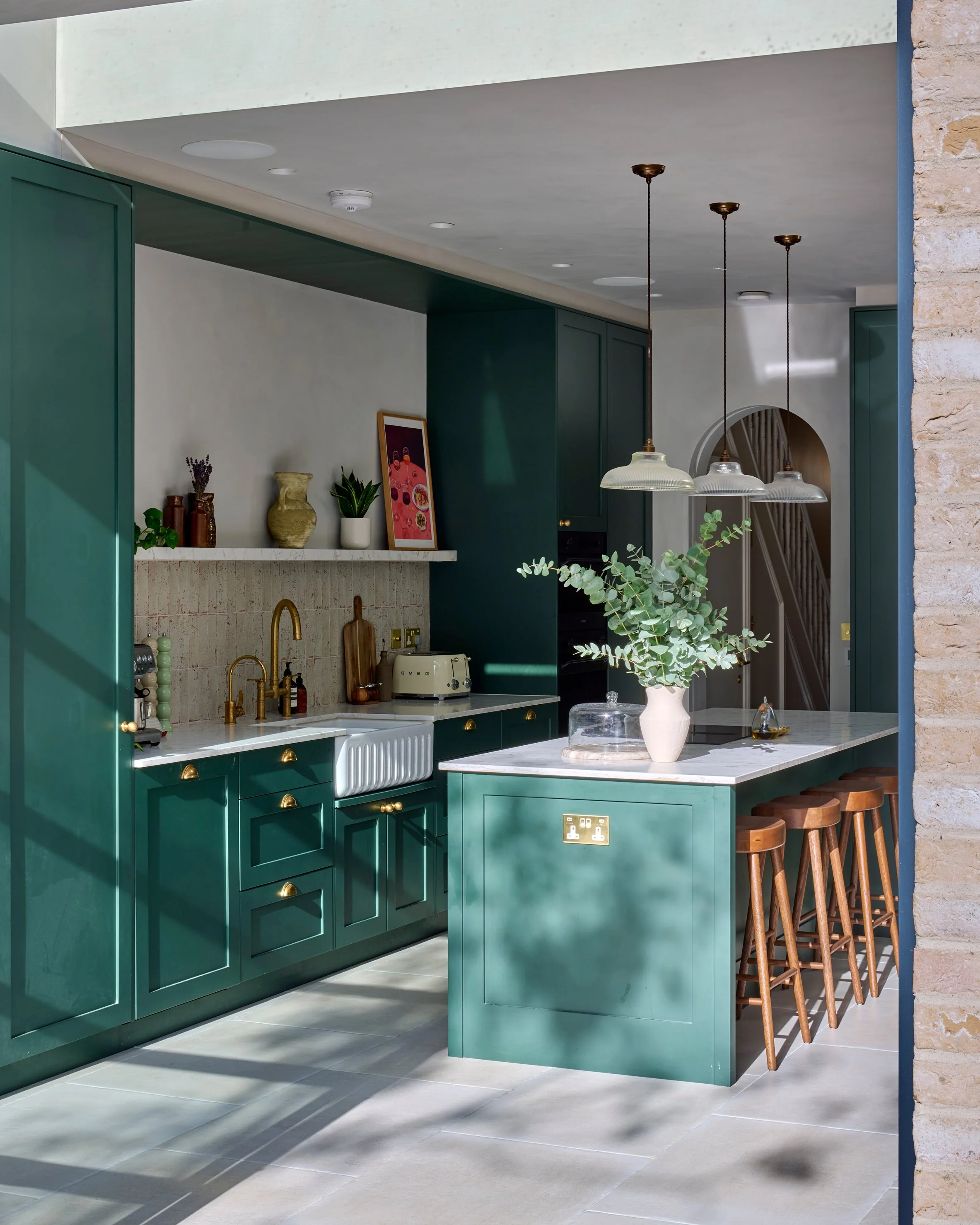 Modern kitchen with green cabinets, marble island, pendant lights, potted plant, and decorative items on a shelf