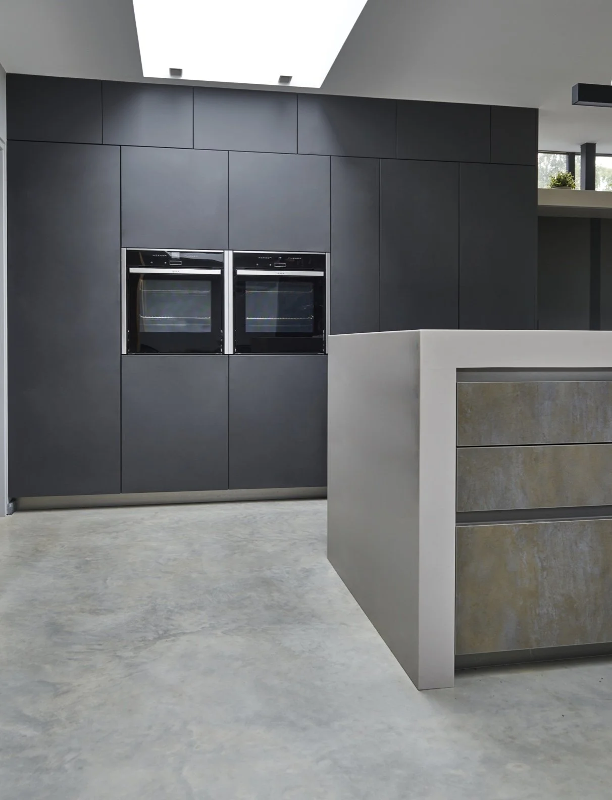 Modern kitchen with black cabinetry, built-in ovens, an island with a beige and yellow patterned drawer front, and a concrete floor.