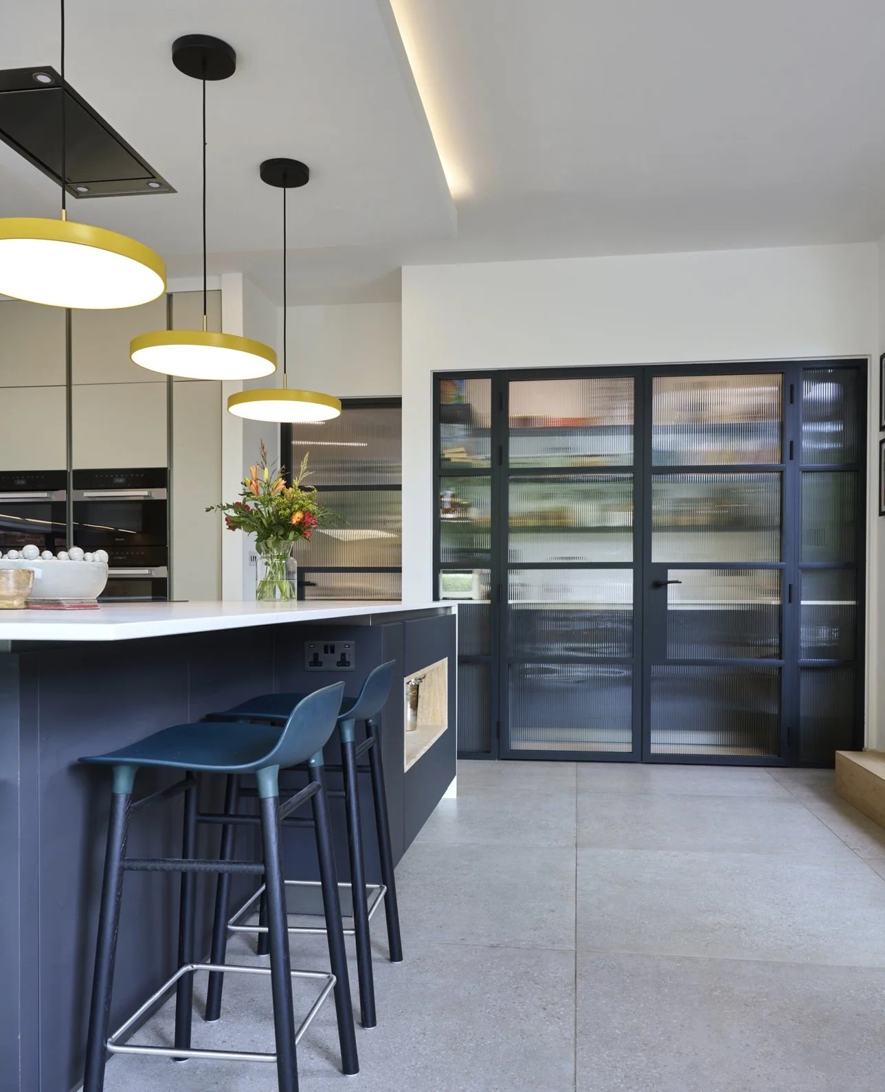 Modern kitchen with black and white color scheme, pendant lights over a white countertop, a flower vase, and a sliding glass door.
