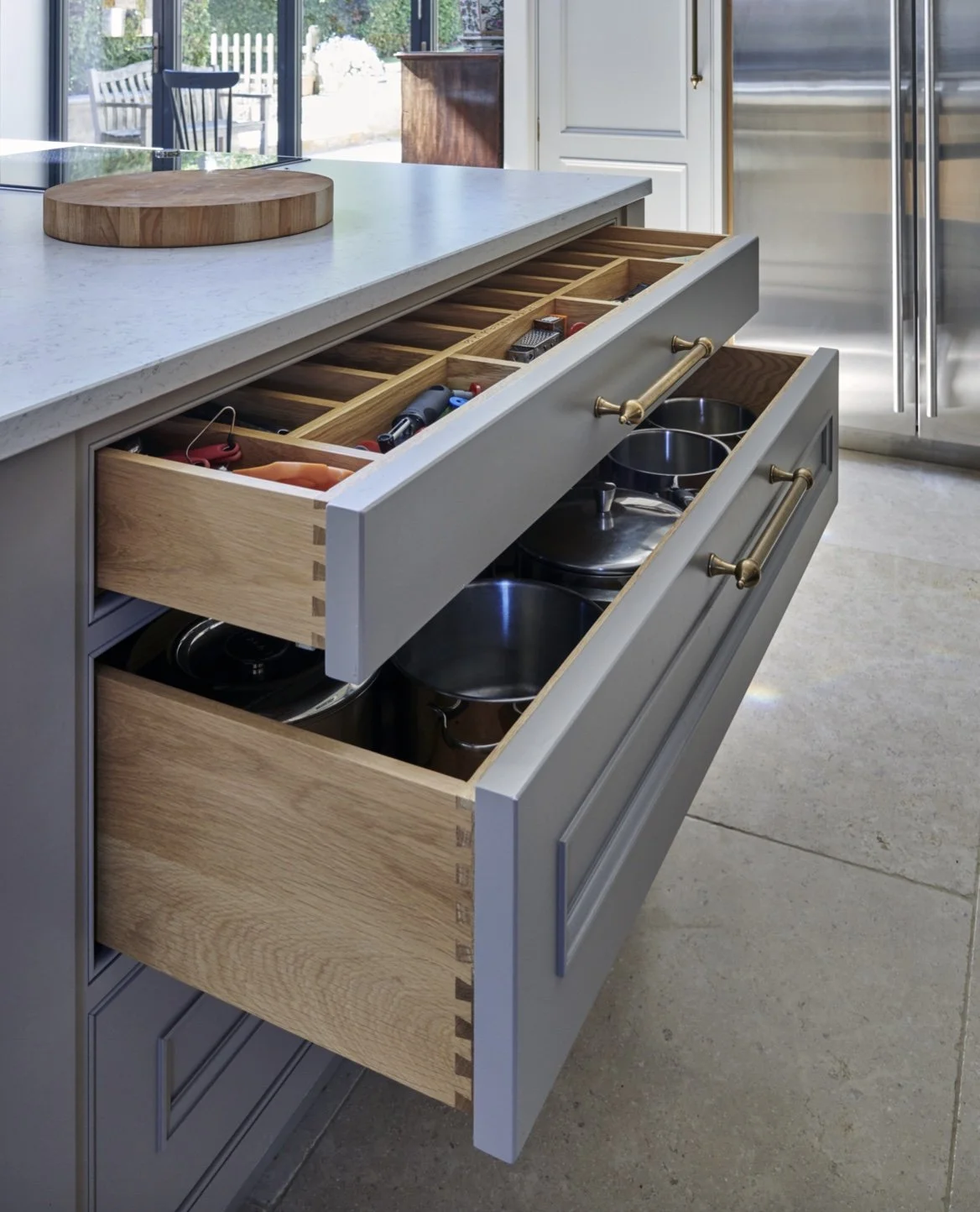 Open kitchen drawers containing pots and pans, with a marble countertop and a cutting board on top.
