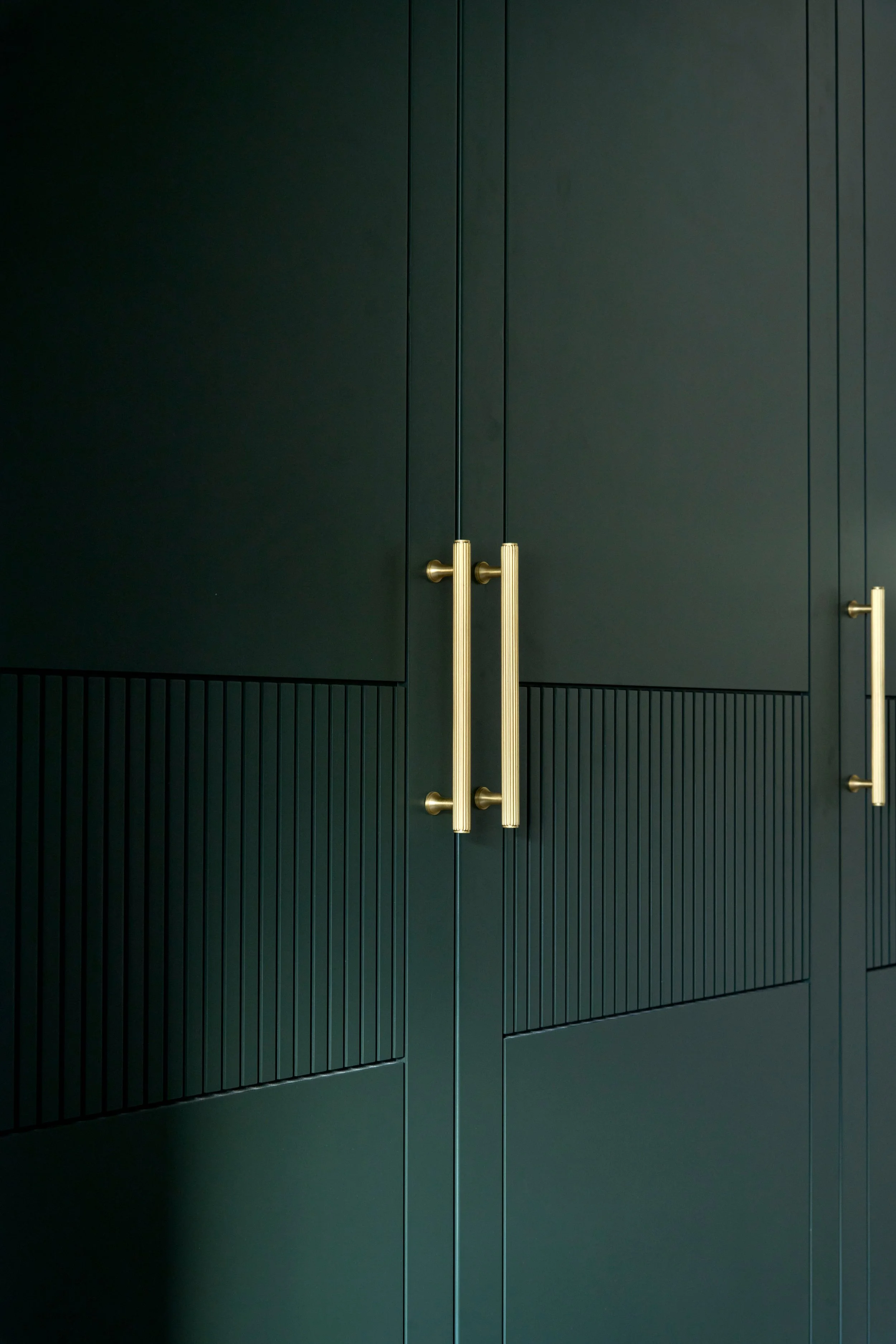 A dark green cabinet with vertical panels and two gold handles in the center.