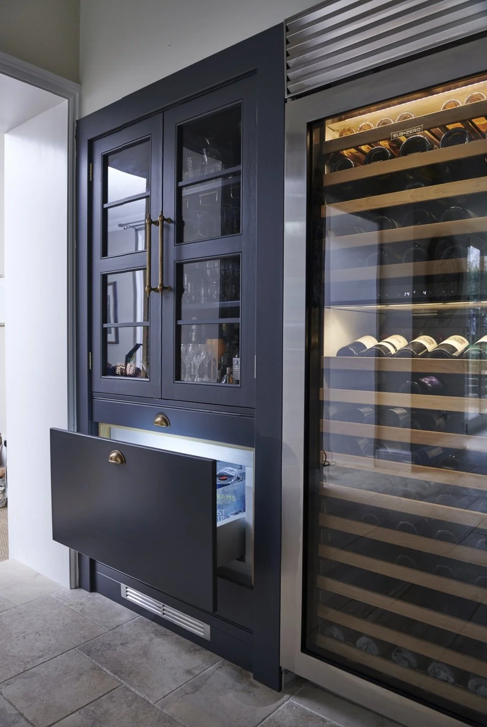 A black wooden cabinet with glass doors and gold handles next to a large wine cooler filled with wine bottles.