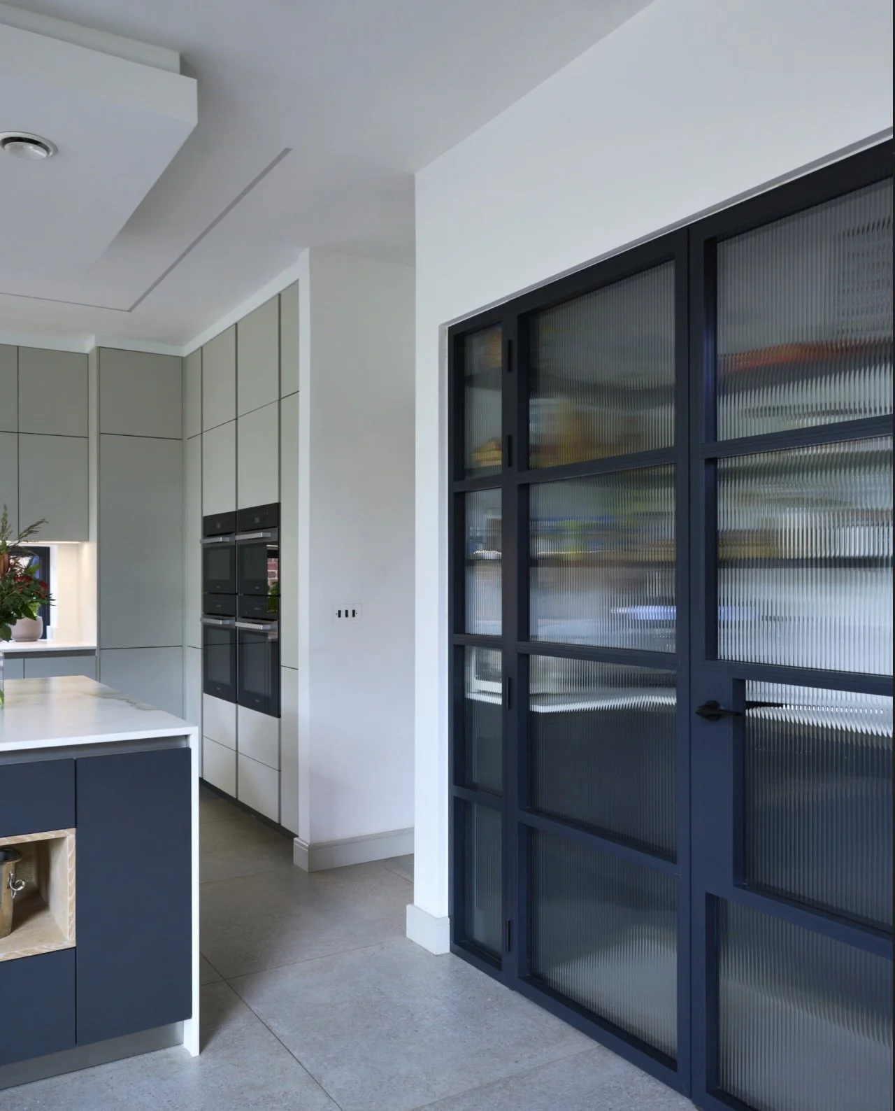 Modern kitchen with white cabinets, built-in oven, and a blue sliding door with textured glass panels.
