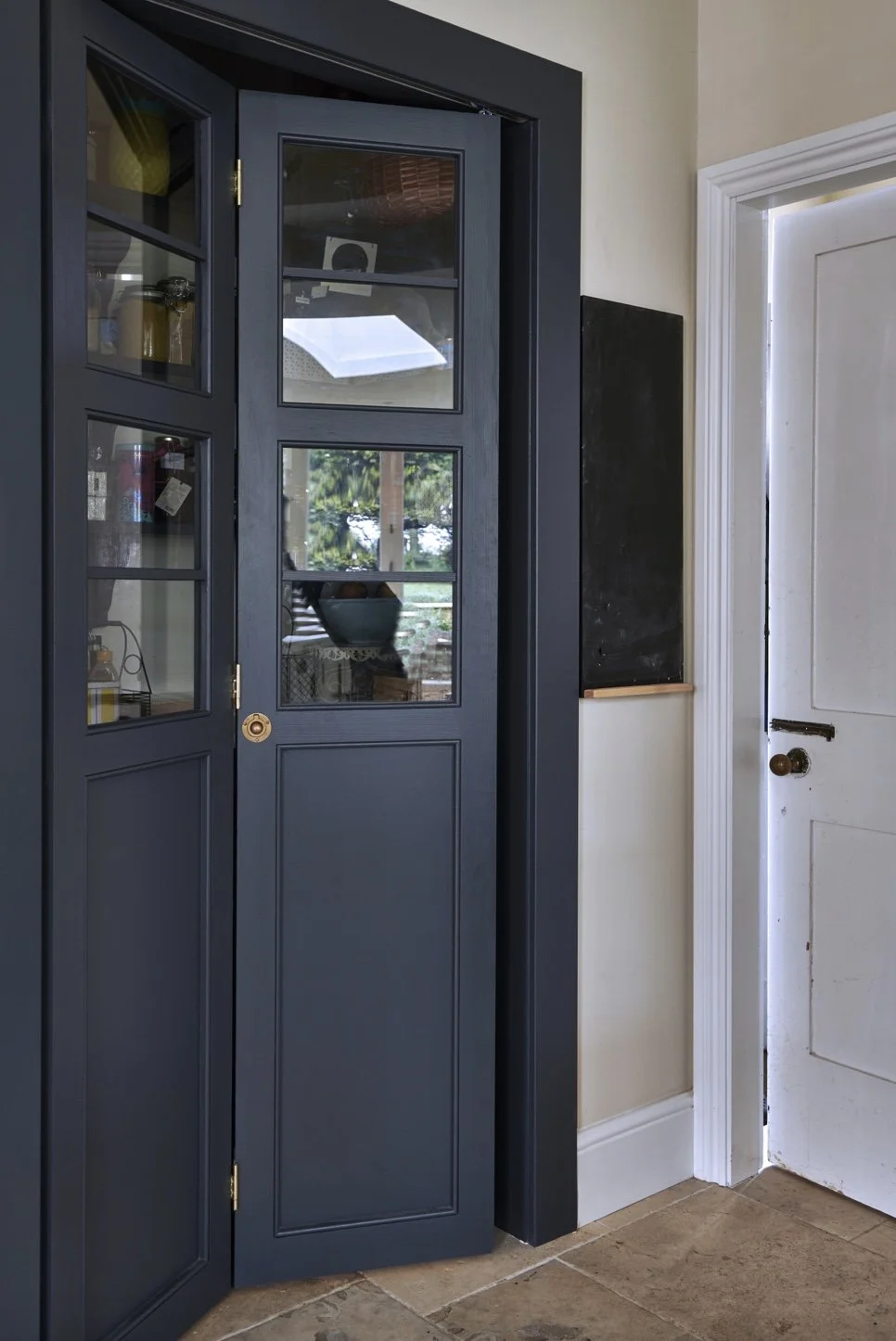 Interior view of a blue wooden and glass-door cabinet next to a white door with a black chalkboard on the wall beside it, in a room with beige walls and tiled flooring.