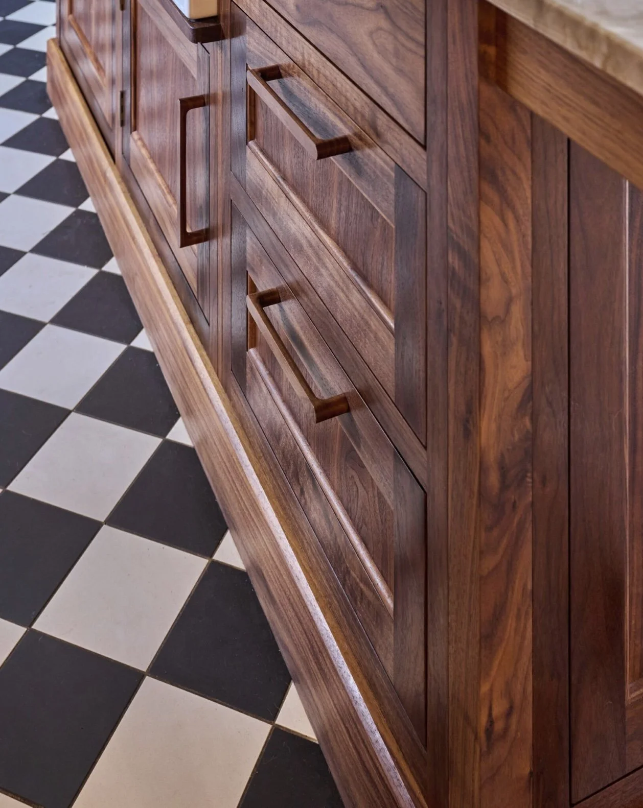 Close-up of a wooden cabinet with drawers and a checkered black and white floor.