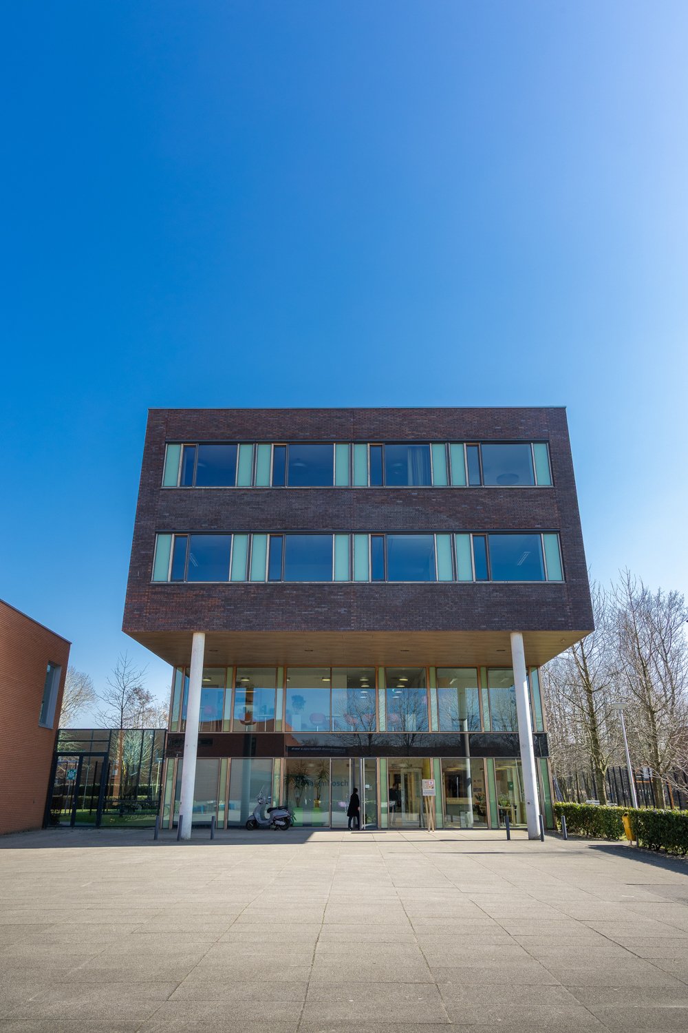 Modern kantoorgebouw met drie verdiepingen, grote glazen ramen en een open ingang op de begane grond onder een heldere blauwe hemel.
