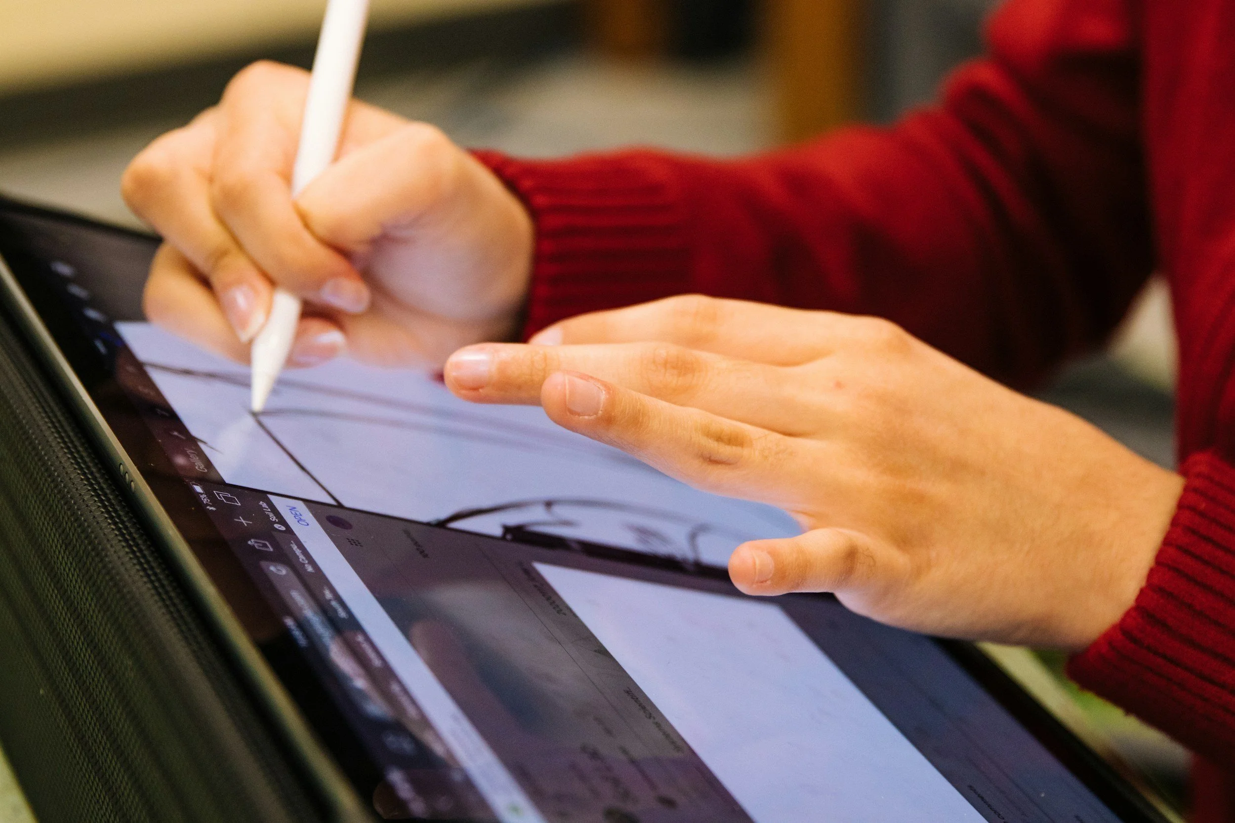 Een persoon tekent met een stylus op een tablet met een rood trui aan.