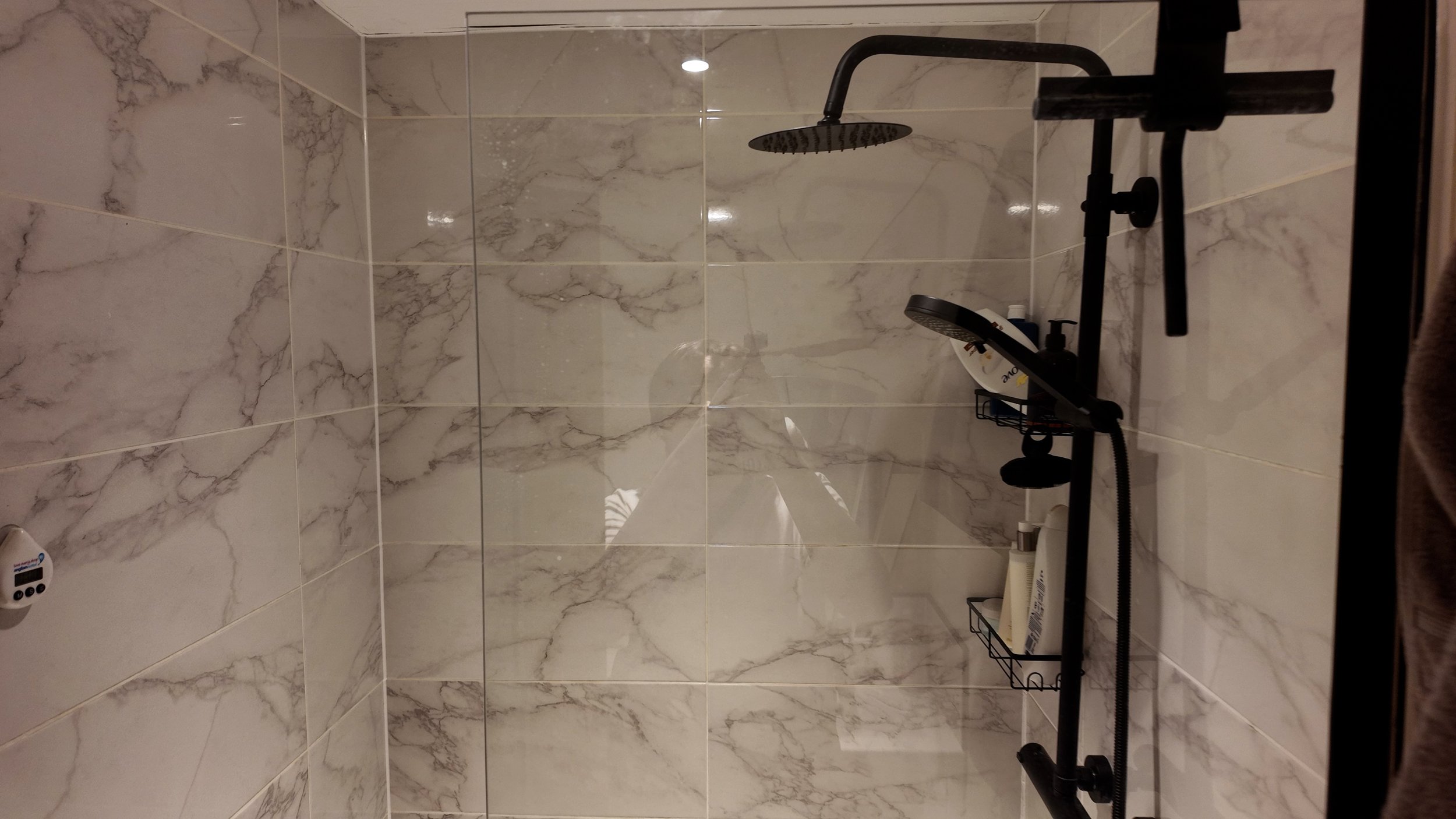 Shower area with marble tiles, black shower fixtures, and a shower shelf with toiletries.