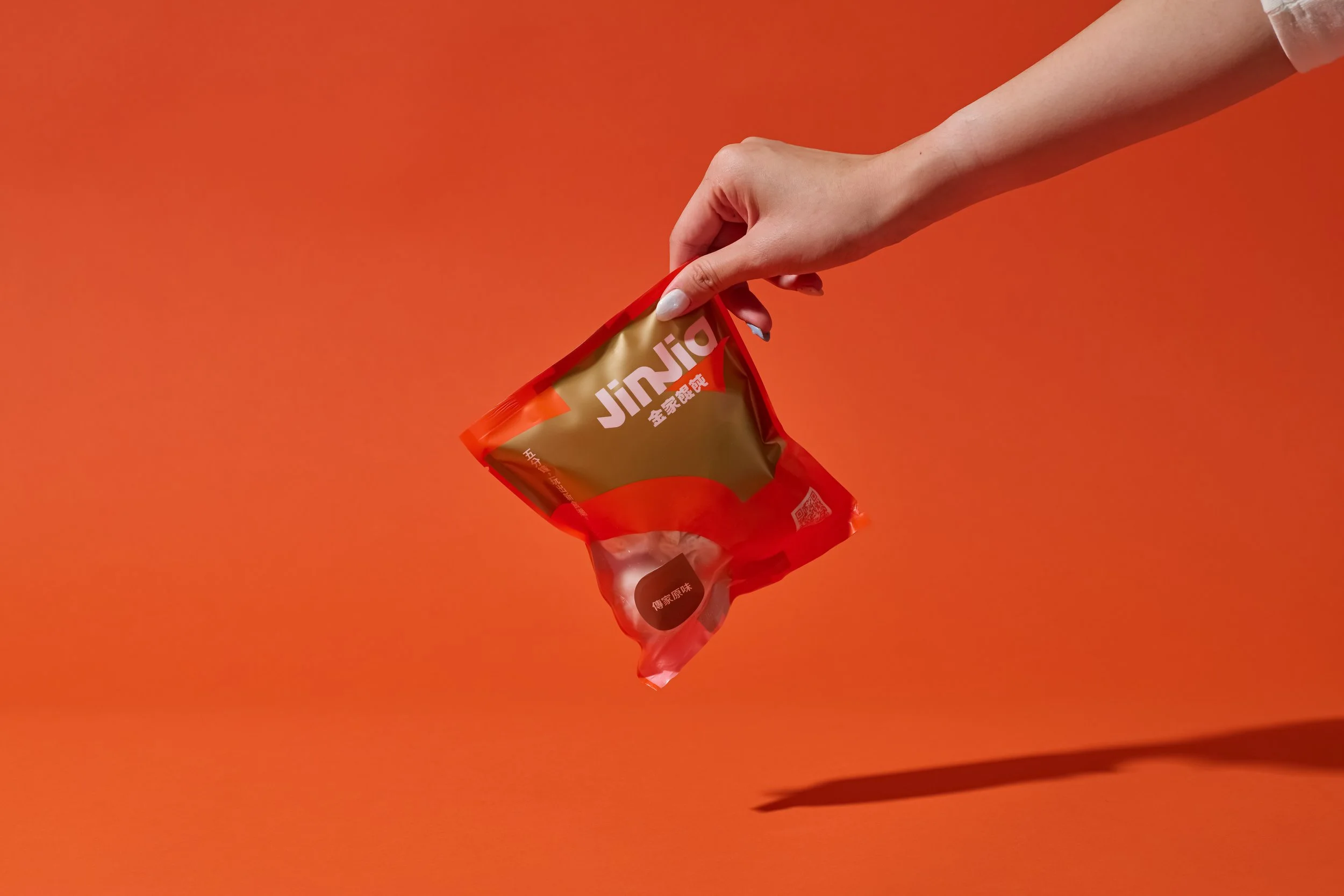 A hand holding a red and gold Jinjia snack package against an orange background.