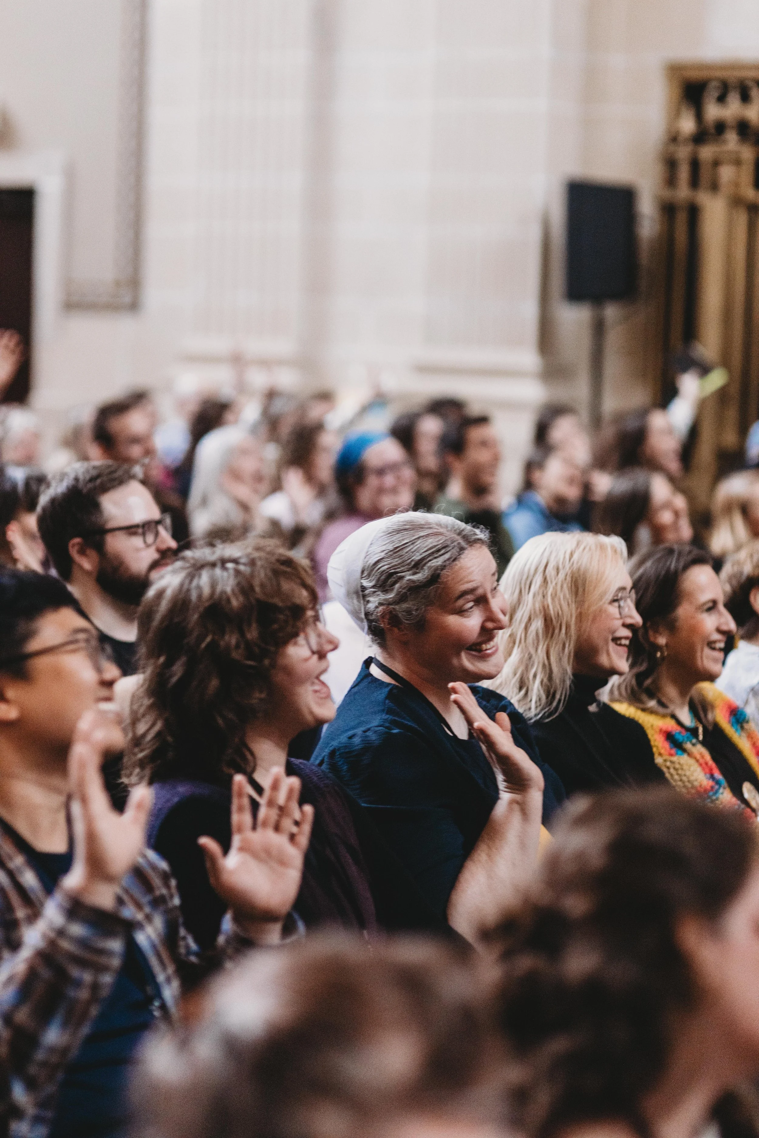 An audience at a crowded event enjoying a presentation or performance, with various people smiling and some raising their hands.