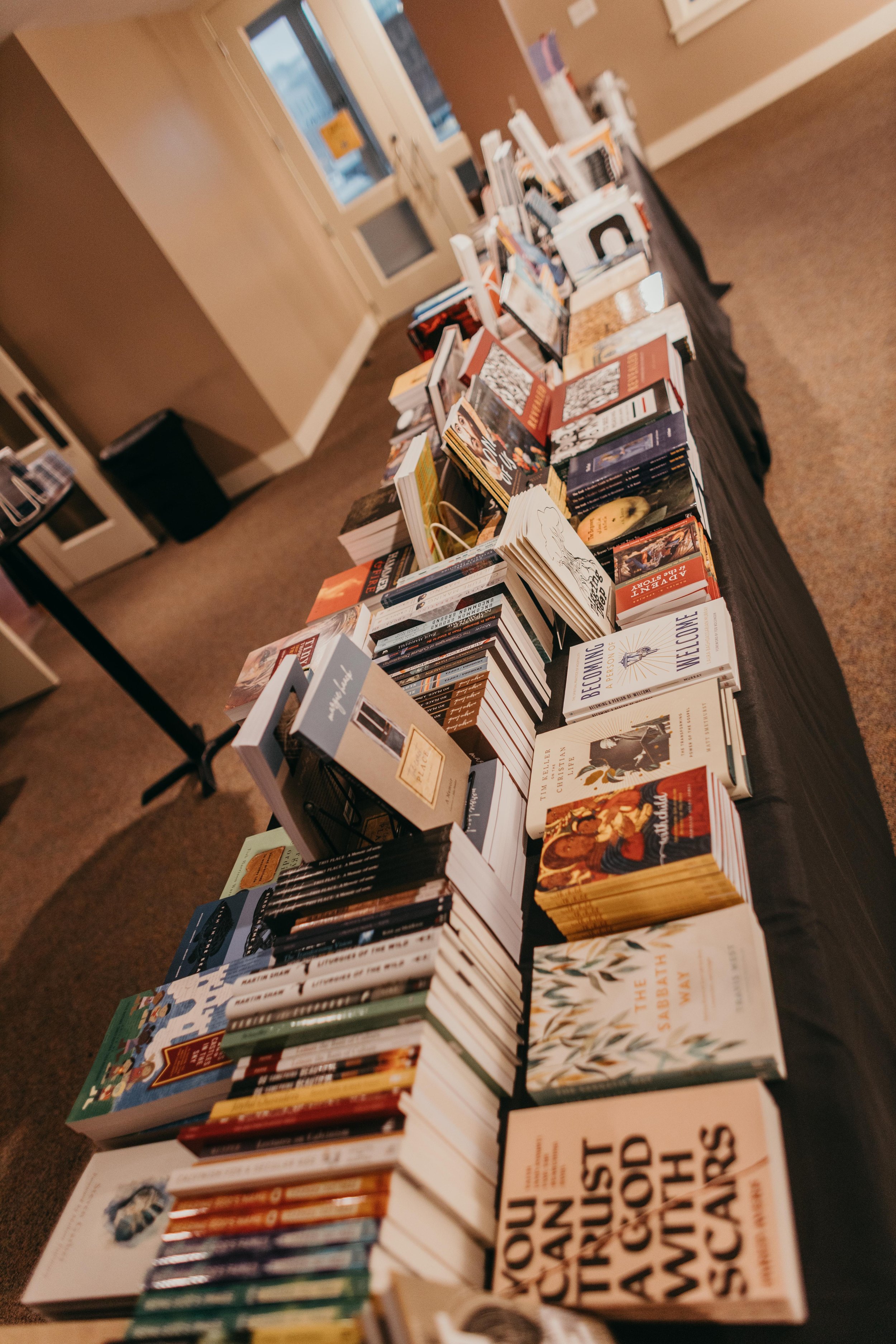 Table with books displayed for sale, inside a room with a glass door and windows in the background.
