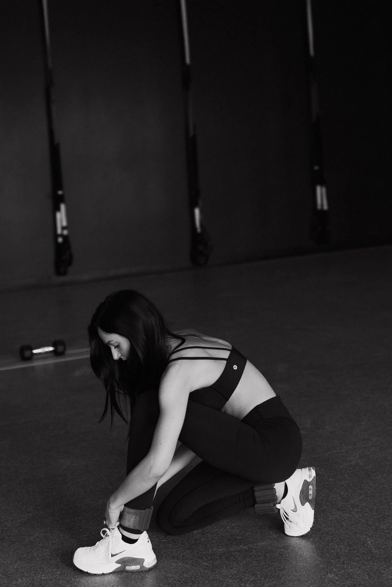 A woman in workout clothes tying her shoelaces in a gym.