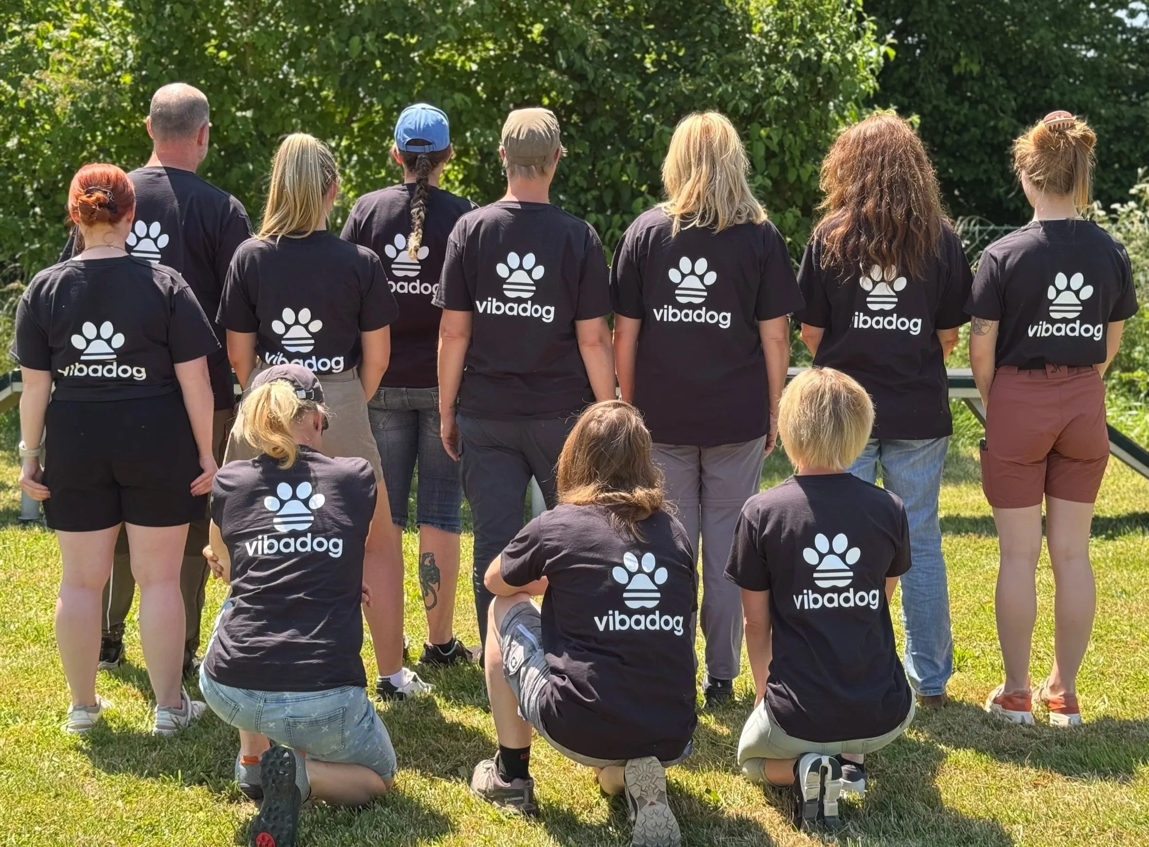 Gruppe von ViBaDog-Community-Mitgliedern in schwarzen ViBaDog-Shirts mit Pfotenlogo bei einem gemeinsamen Treffen im Freien.