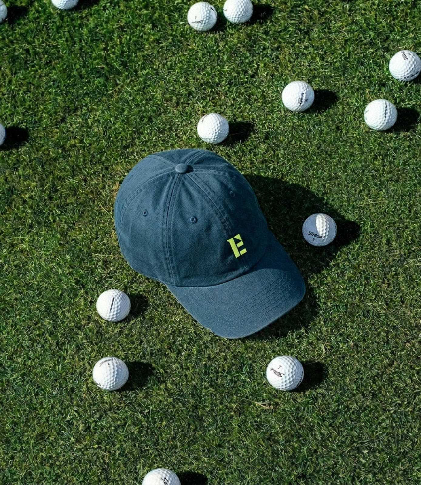 Golf branding for Intuitive Edge featuring embroidered logo on cap surrounded by golf balls on grass, showcasing sports brand identity design