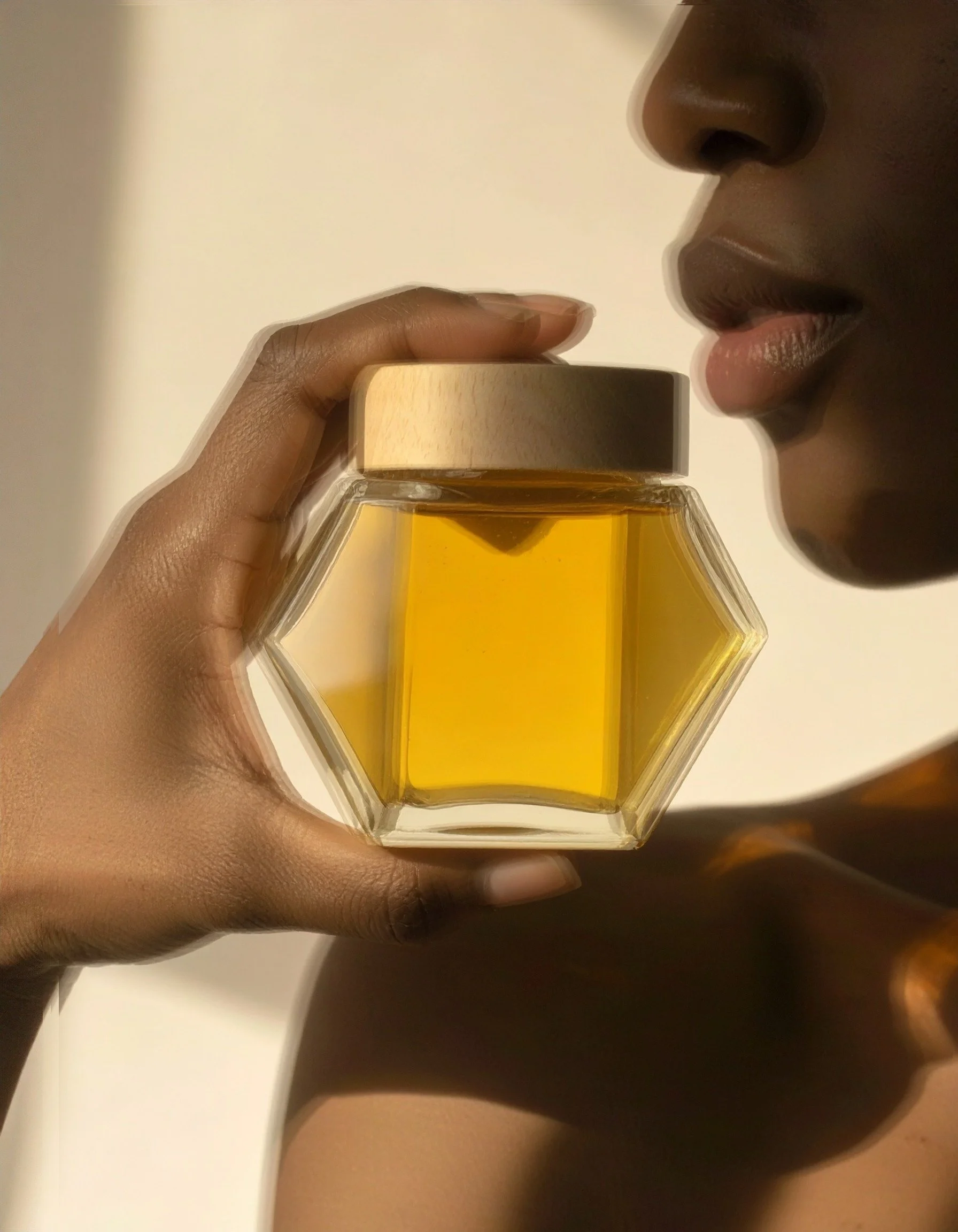 Luxury honey product photography featuring a Black woman holding a geometric glass honey jar in warm golden light, styled for a premium wellness and lifestyle brand.