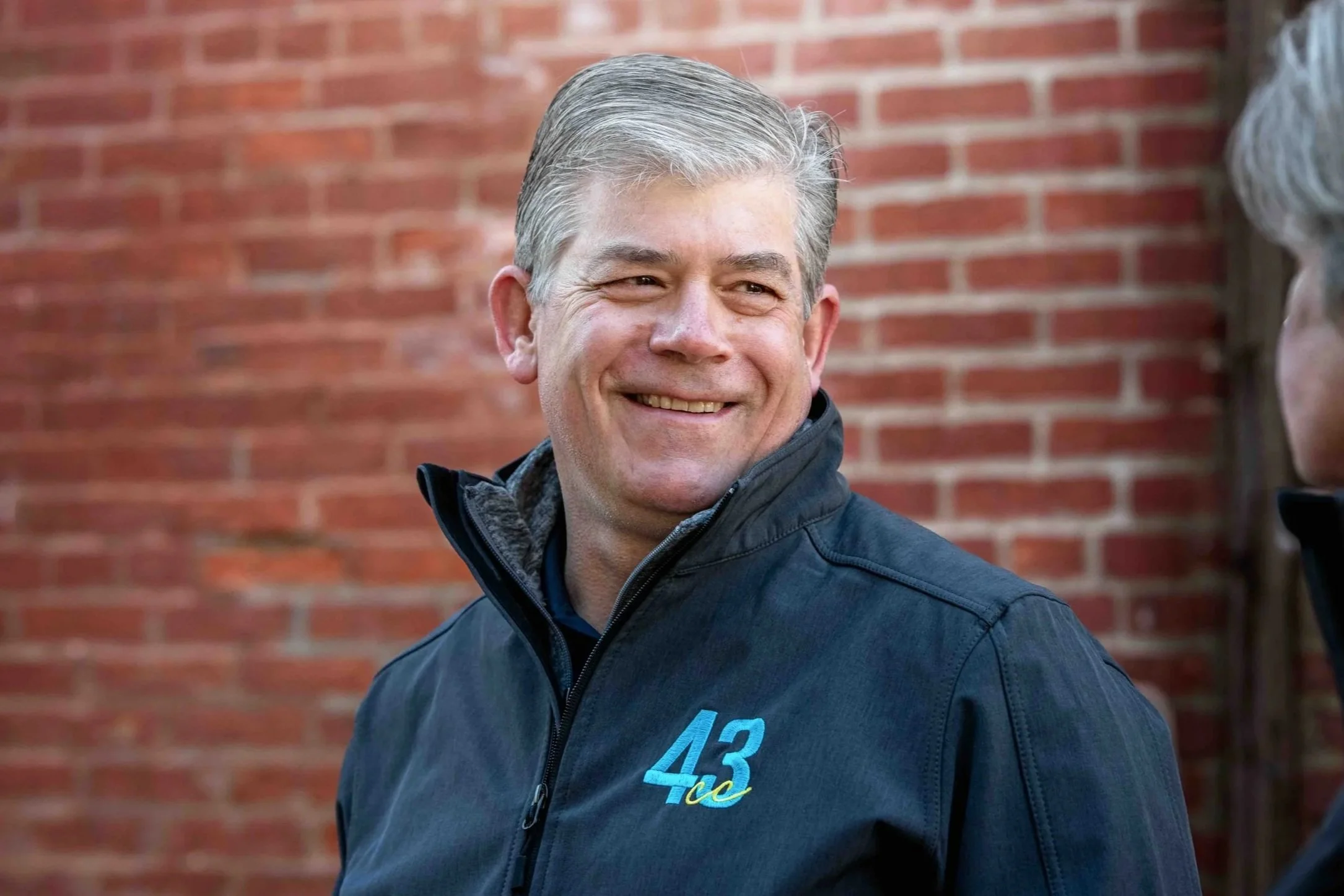 Smiling person with grey hair against brick background.