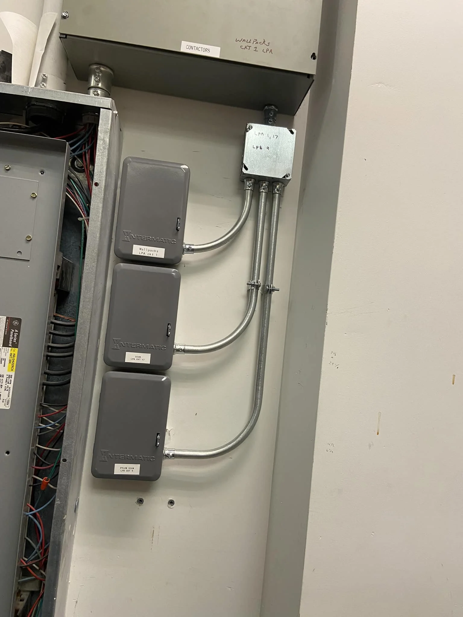 Electrical panels and wiring inside an electrical cabinet with circuit boxes labeled 'Wallpack LPA' and 'Contactors' mounted on a wall.