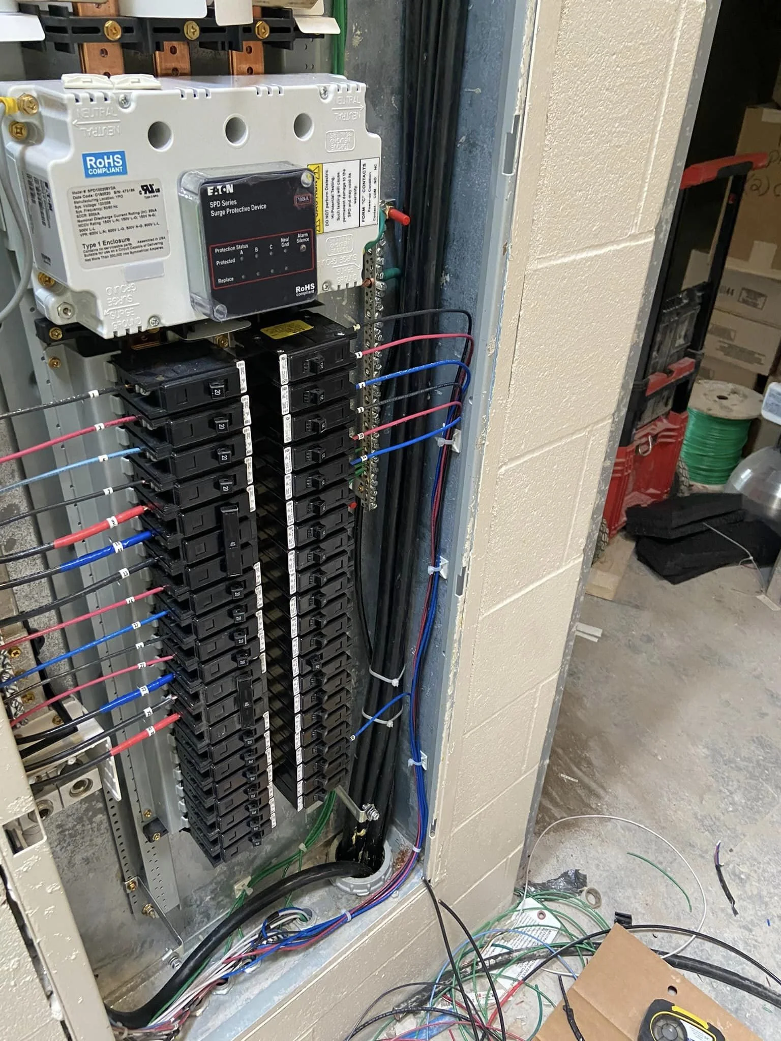 Electrical panel with circuit breakers, wiring, and a surge protector device inside a utility closet.