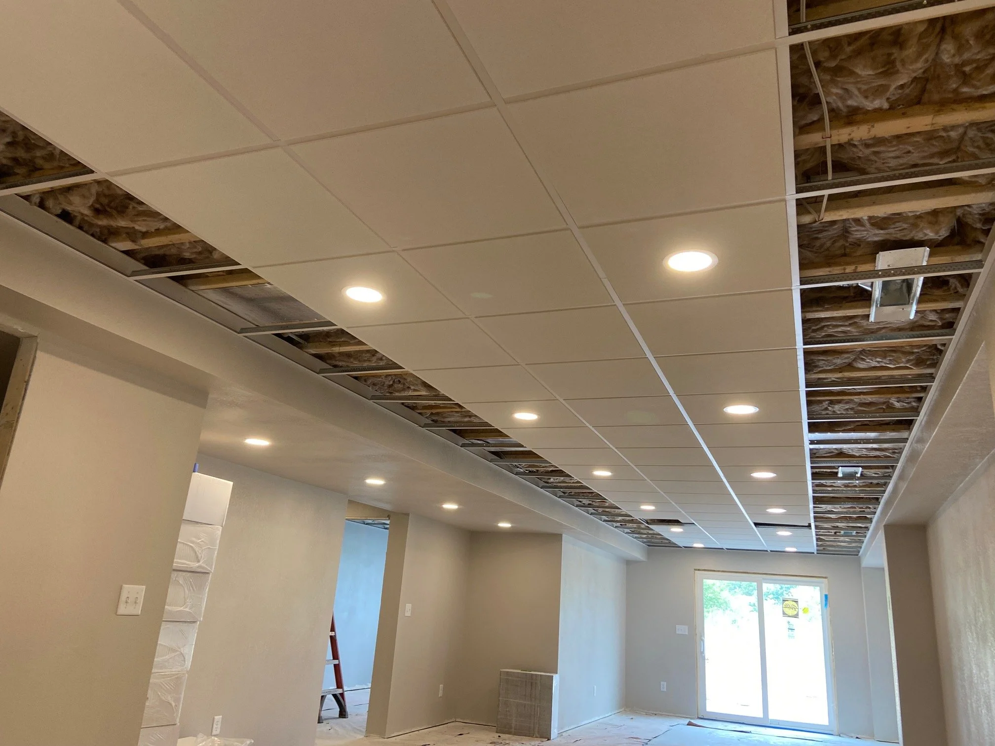Living room with in-progress ceiling construction, recessed lighting, and sliding glass doors with patio view.