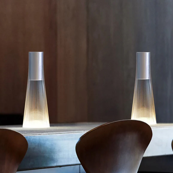Two Pablo Candel Lamps glowing on a modern wooden table