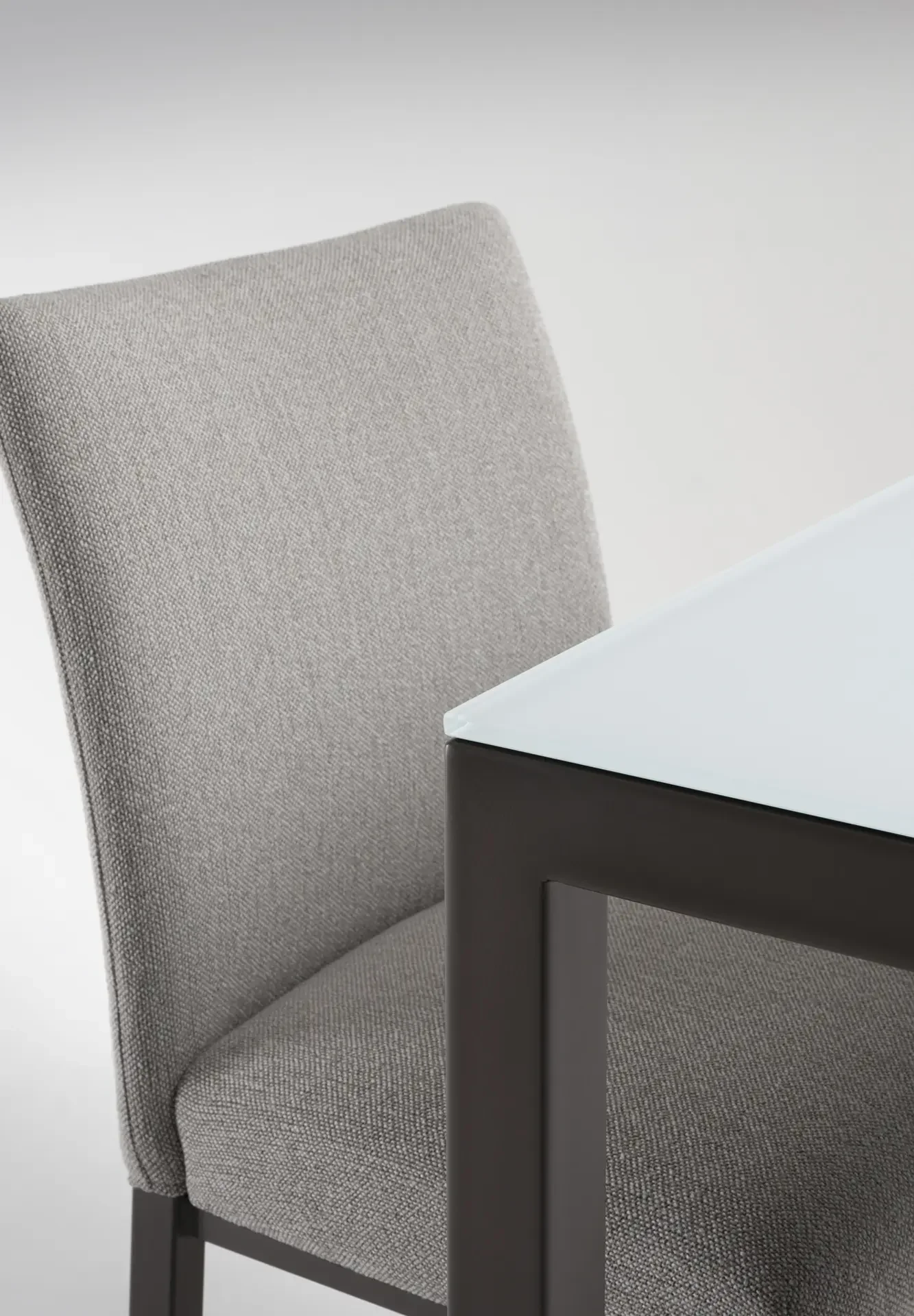 Close-up of upholstered dining chair next to Trica Cubo Dining Table with glass top