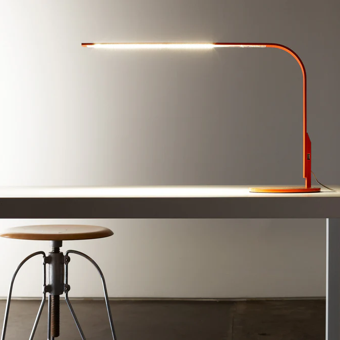 Orange Pablo Lim 360 Task Light illuminating a desk workspace
