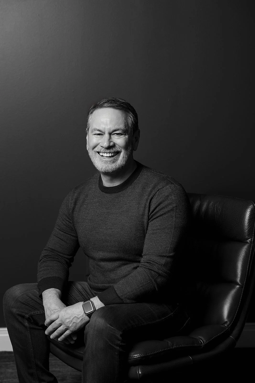 Smiling man standing next to a chair with a blue wall and abstract art in the background.