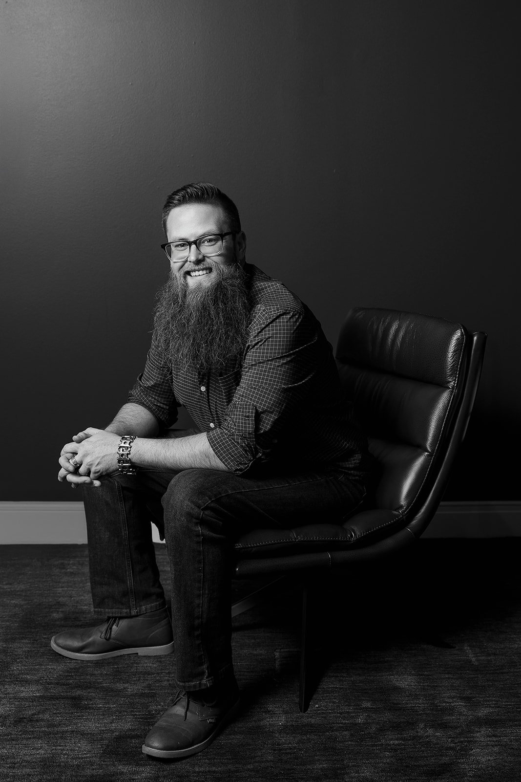Man sitting in modern chair, smiling, black and white photo in a contemporary setting with simple background 
