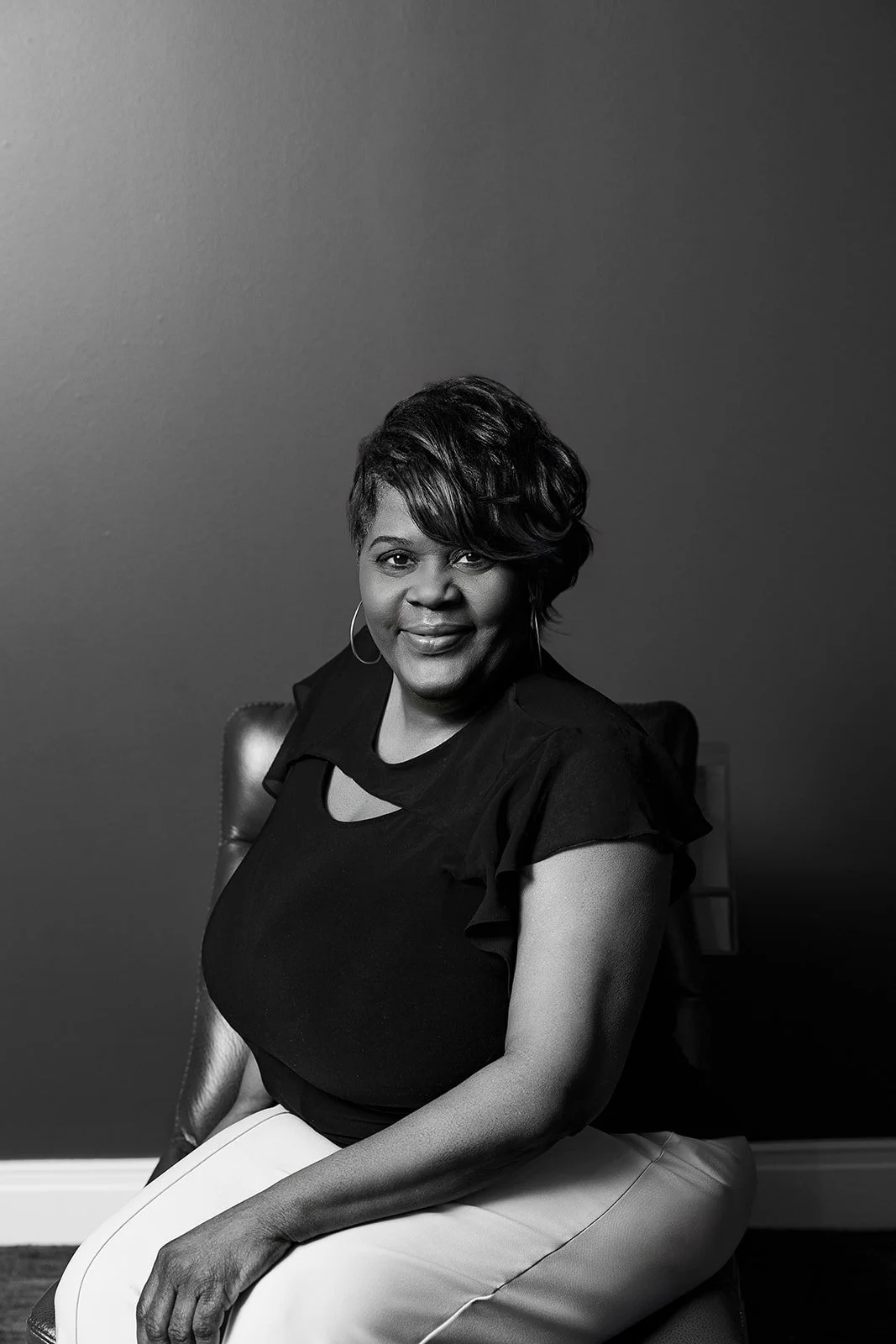 A person sitting on a couch, smiling in a room with purple walls and a modern abstract painting in the background.